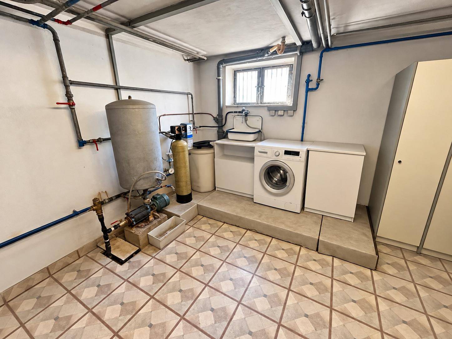 Praktischer Hauswirtschaftsraum im Keller mit Waschmaschine, Warmwasserboiler und technischen Installationen.