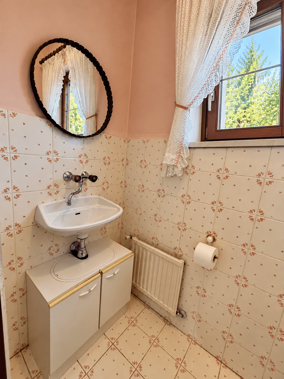 Kleines WC mit Waschbecken, Spiegel und floral gemusterten Wandfliesen.
