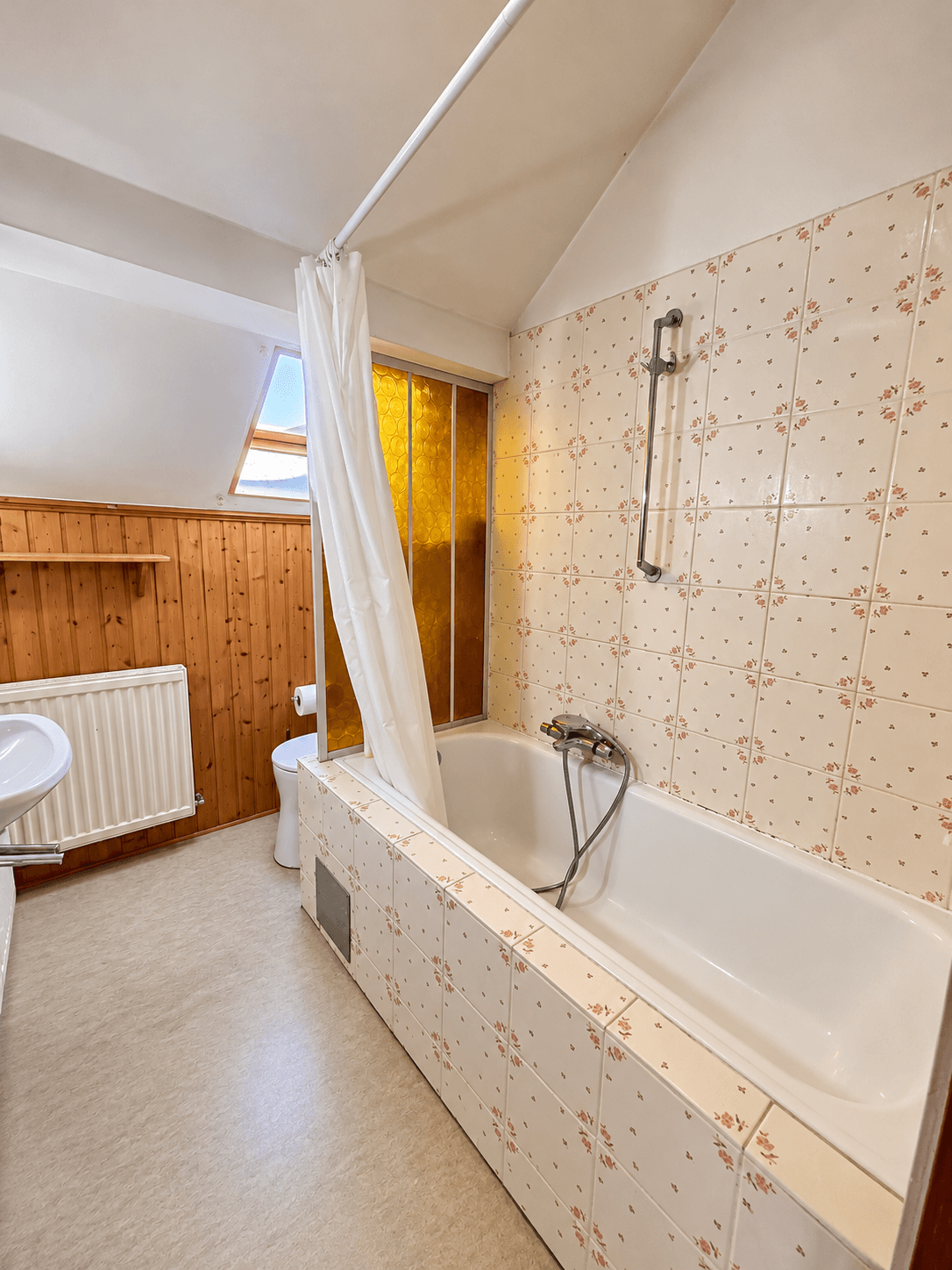 Badezimmer im Dachgeschoss mit Badewanne, Waschbecken und schrägen Decken.