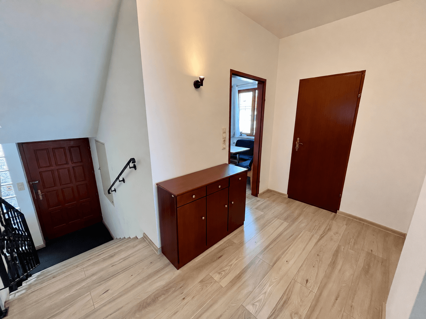 Geräumiger Flur mit Treppenaufgang, Holzkommode und hellem Laminatboden.