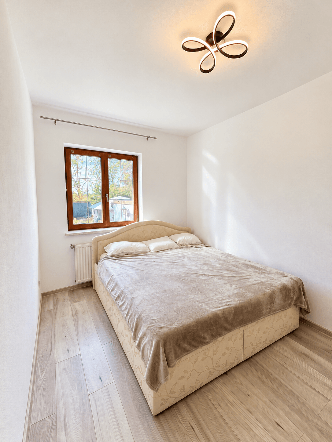 Helles Schlafzimmer mit Doppelbett, Fenster und modernem Laminatboden.