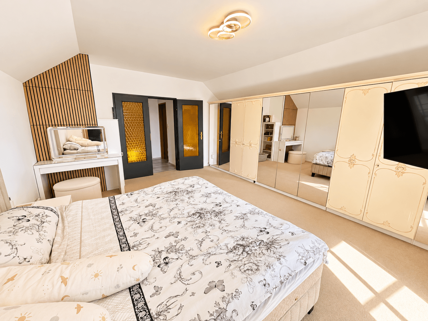 Geräumiges Schlafzimmer mit großem Bett, Spiegelschränken und Schminktisch.