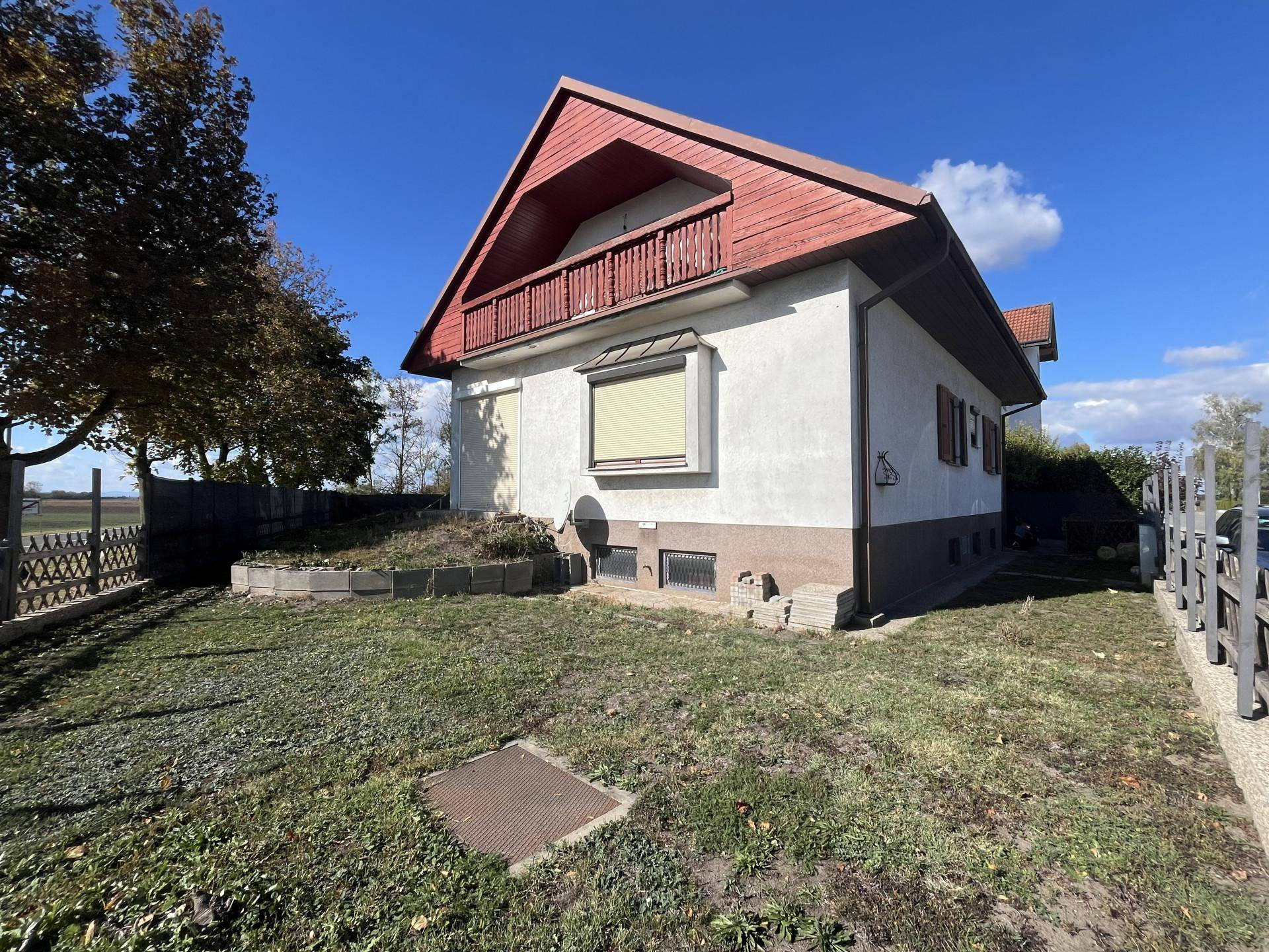 Seitenansicht des Hauses mit kleinem Balkon und umzäuntem Gartenbereich.