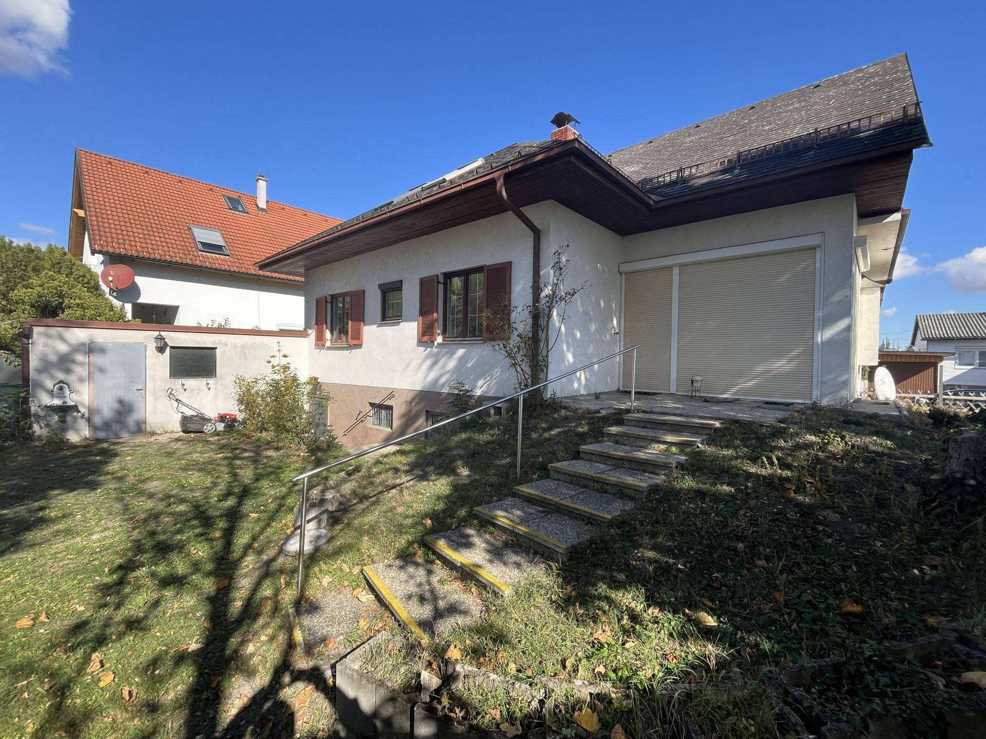 Seitenansicht des Hauses mit Außentreppe, kleinem Schuppen und Garagentor.