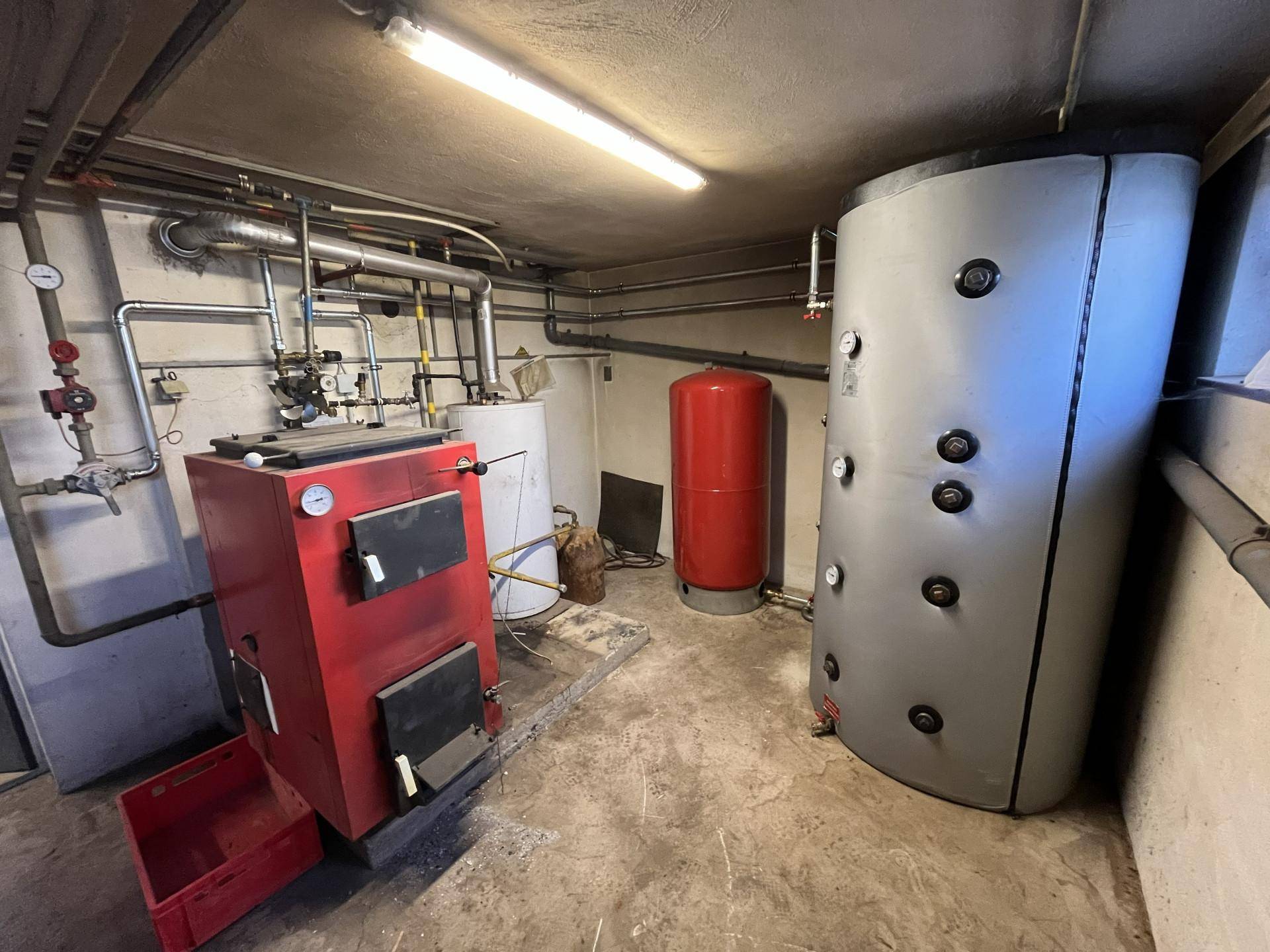 Heizungsraum im Keller mit großem Boiler, Heizkessel und umfangreichen Rohrleitungen.