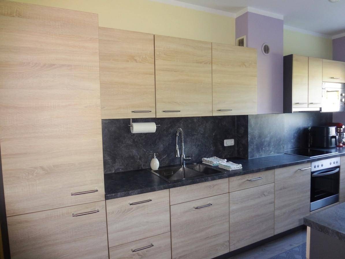 Moderne Einbauküche mit hellen Holzschränken, dunkler Arbeitsplatte und integriertem Spülbecken.