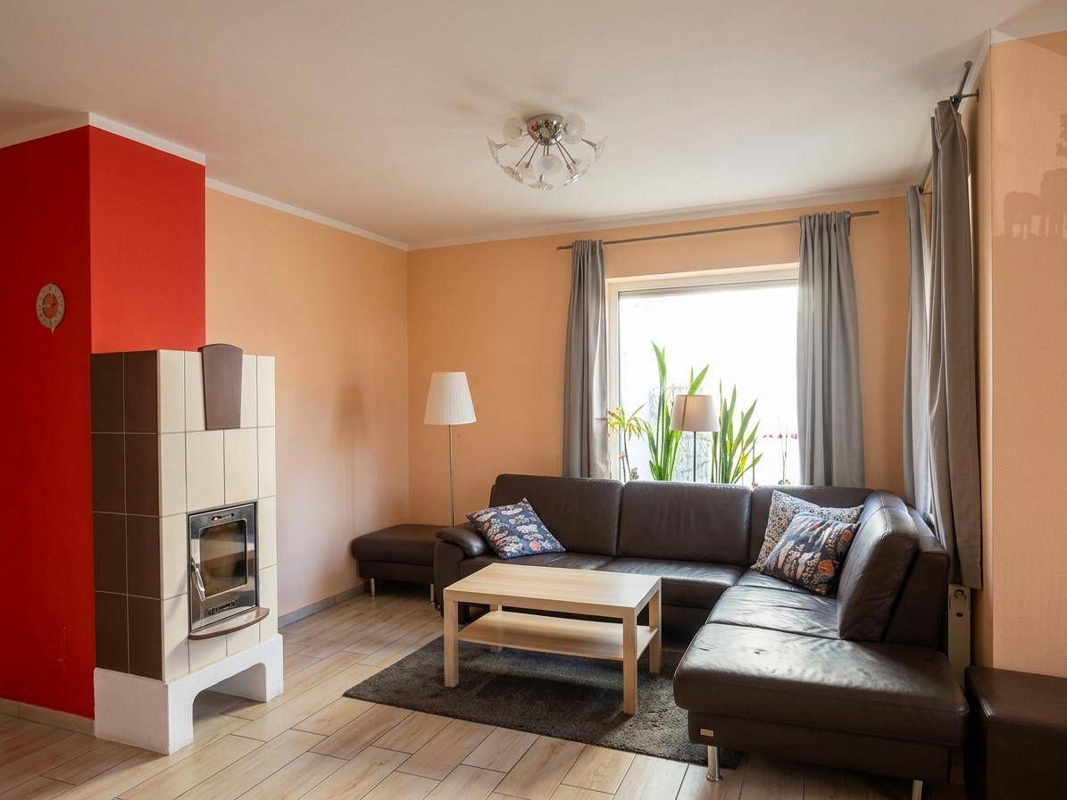 Gemütliches Wohnzimmer mit Kaminofen, Ecksofa und hellem Laminatboden.