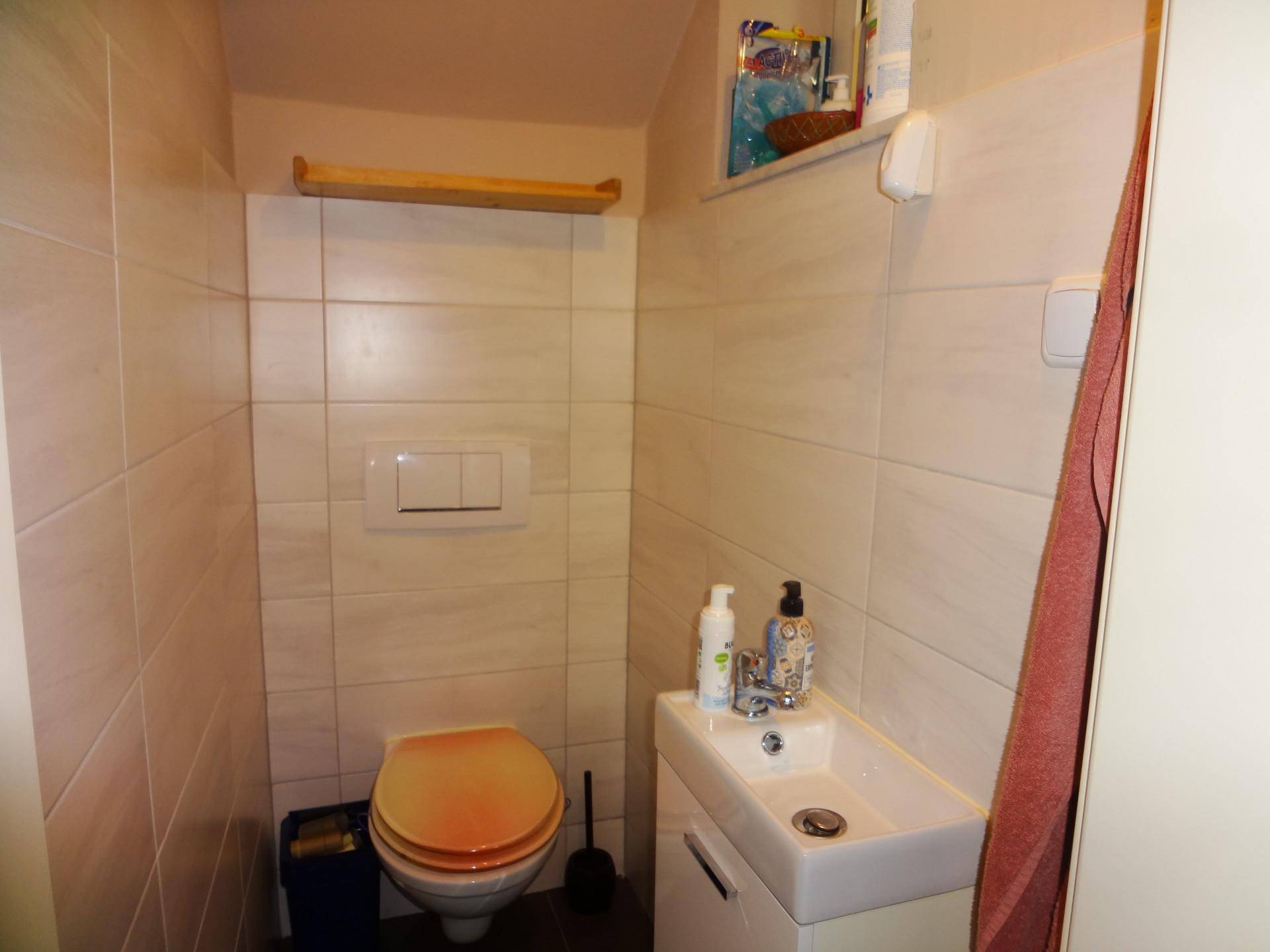 Kleines Gäste-WC mit Wand-WC, Waschbecken und hellen Fliesen an den Wänden.