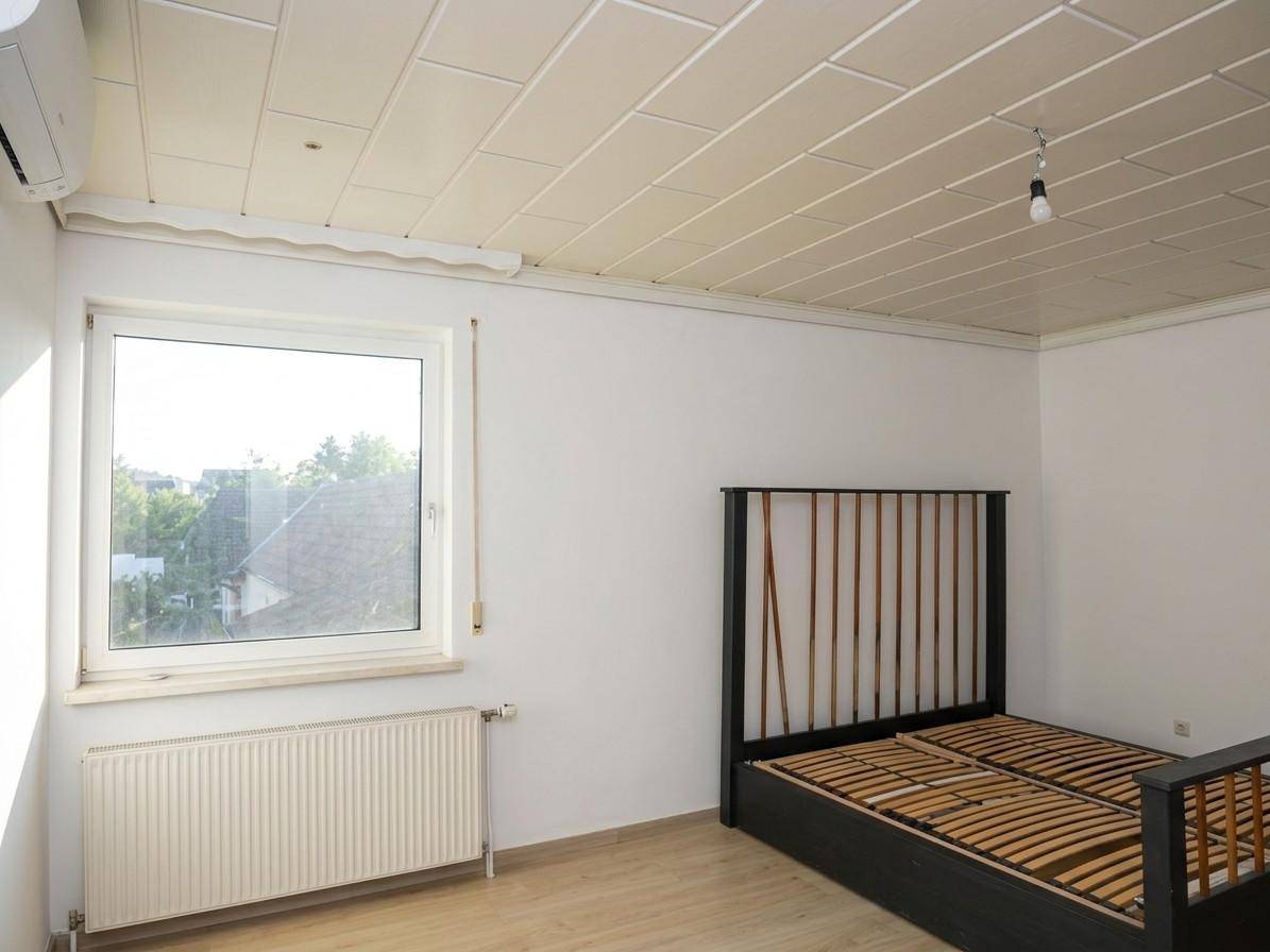 Helles Schlafzimmer mit Doppelbett, Klimaanlage und Blick ins Grüne durch das Fenster.