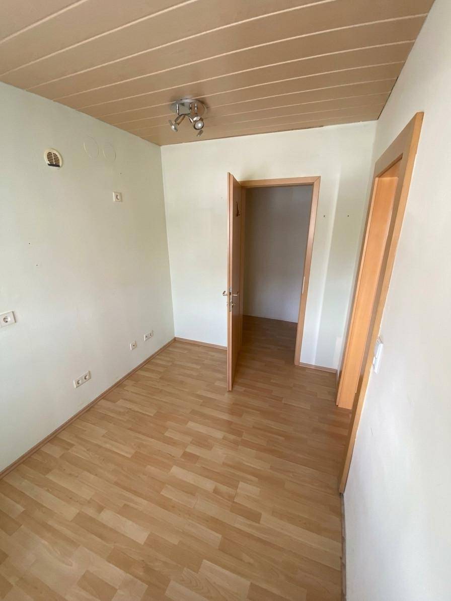 Leeres Zimmer mit Laminatboden, Holzpaneeldecke und hellen Wänden, bereit zur individuellen Gestaltung.