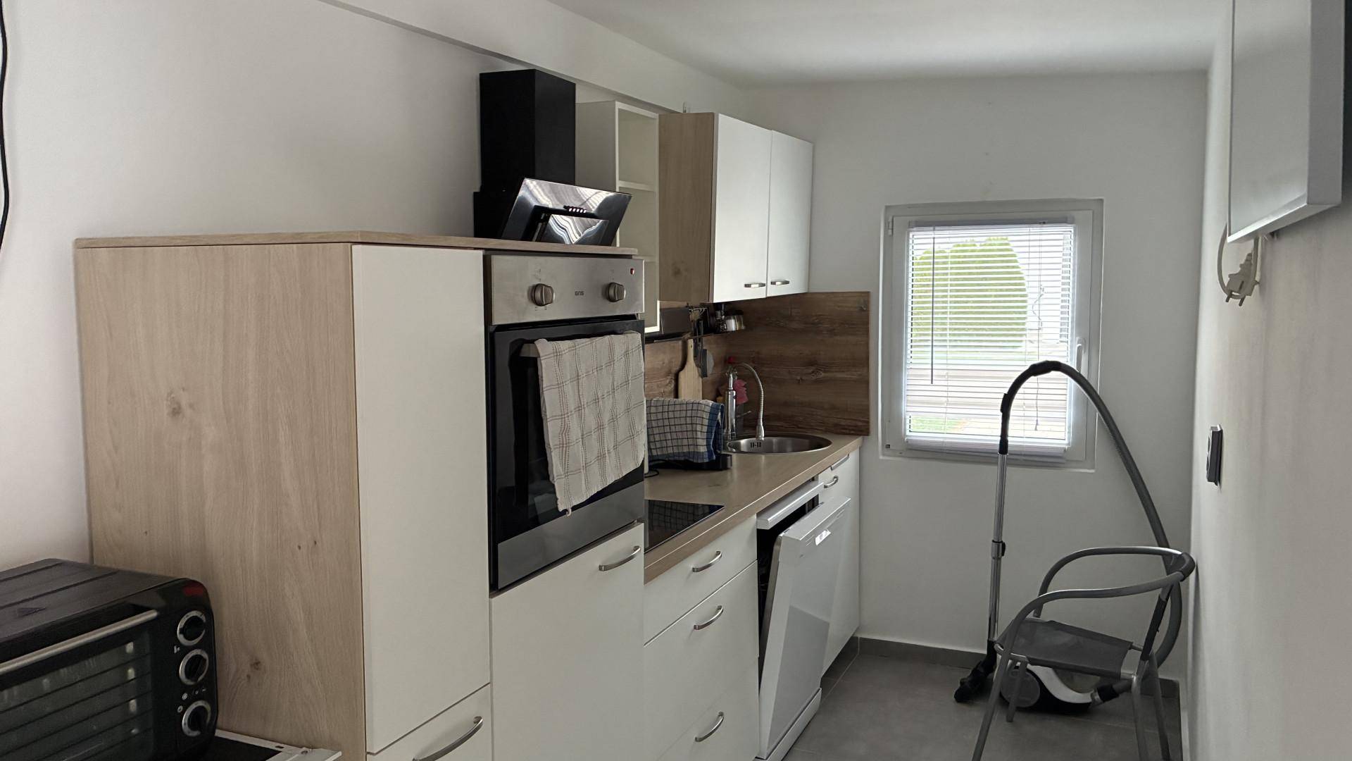 Kleine Küche mit weißen und holzfarbenen Schränken, Ofen und Spülmaschine.
