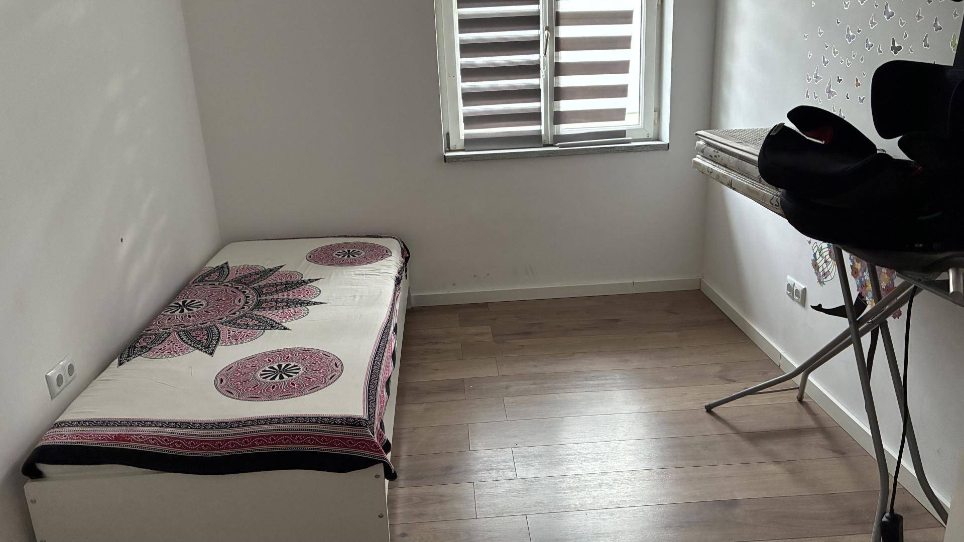Schlafzimmer mit Einzelbett, Holzboden und einem Fenster mit Jalousien.