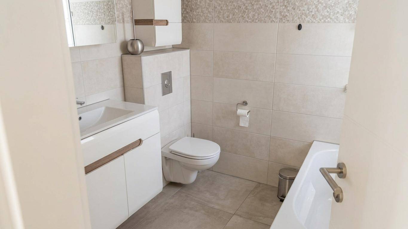 Modernes Badezimmer mit hellen Fliesen, Waschtisch, Toilette und Badewanne.