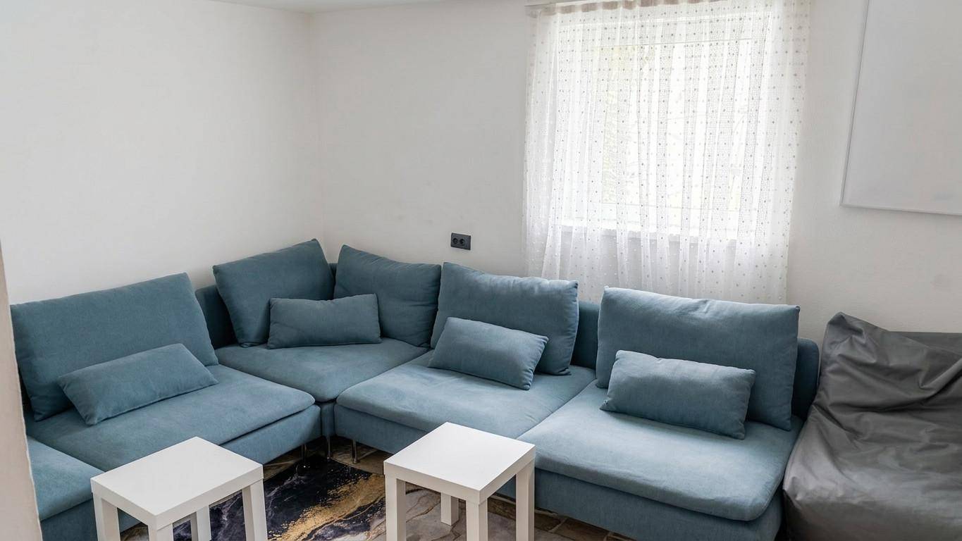 Gemütliches Wohnzimmer mit einem großen blauen Ecksofa und kleinen Beistelltischen.