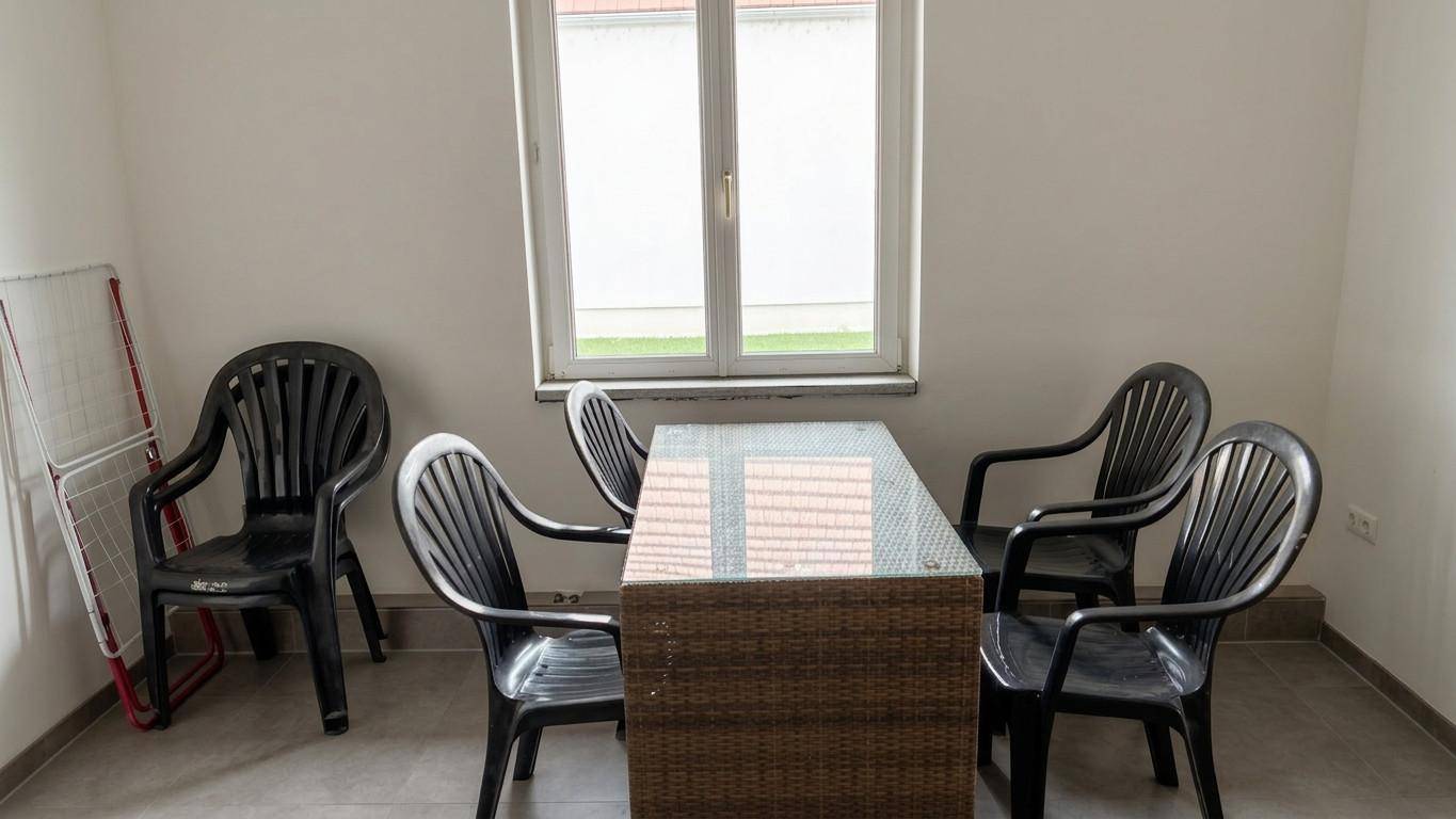 Einfacher Essbereich mit einem Glastisch und schwarzen Plastikstühlen.