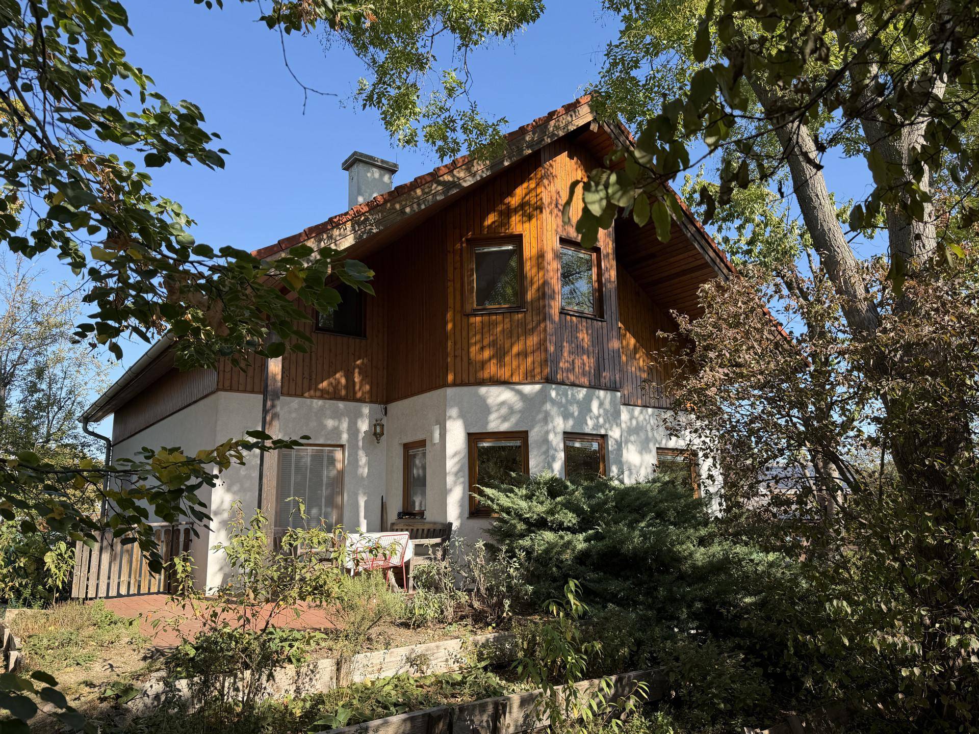 Freistehendes Haus mit traditionellem Satteldach und Holzfassade, eingebettet in eine grüne Umgebung.