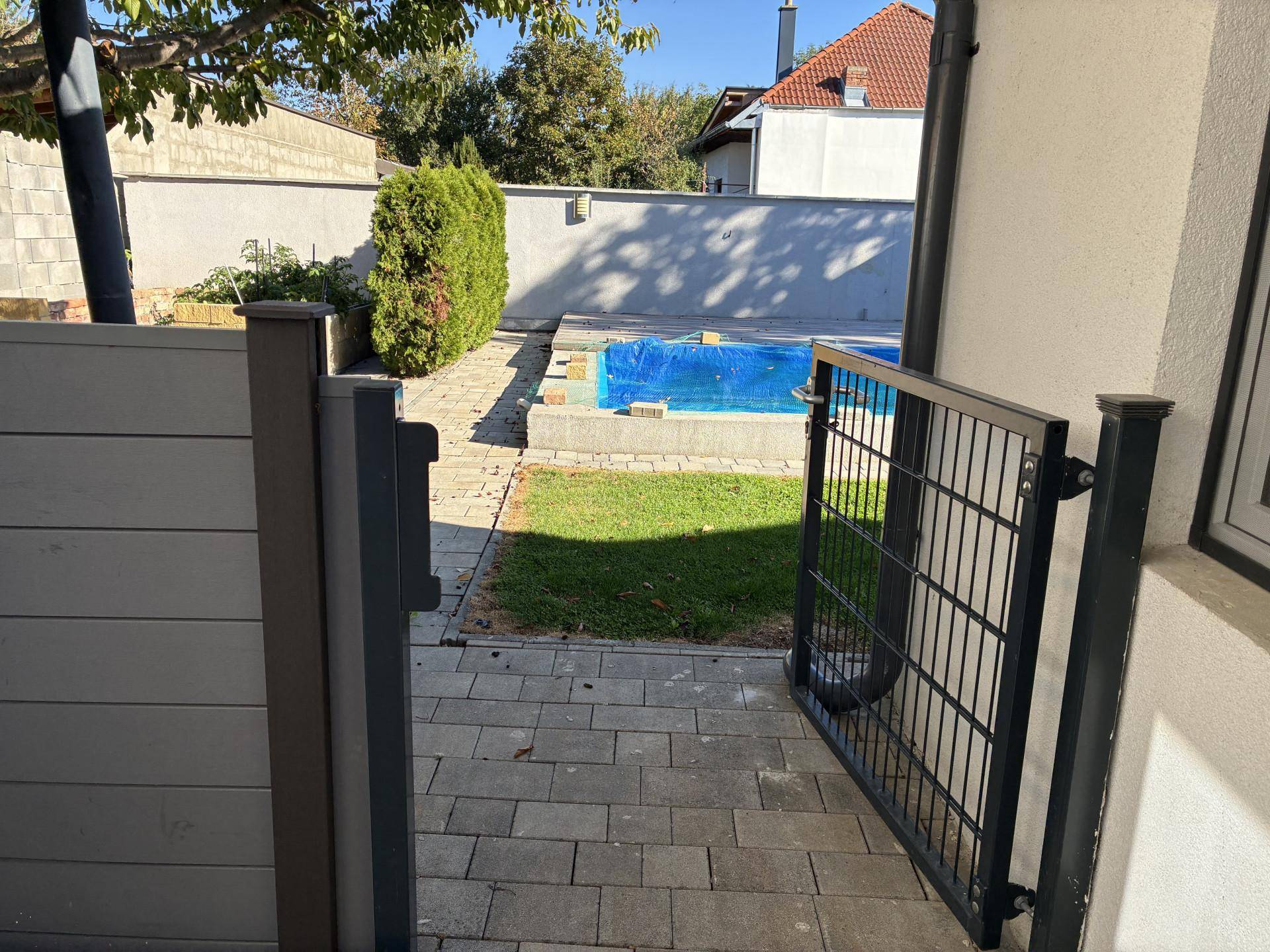Blick durch ein Gartentor auf den hinteren Bereich mit Rasenfläche und Pool.