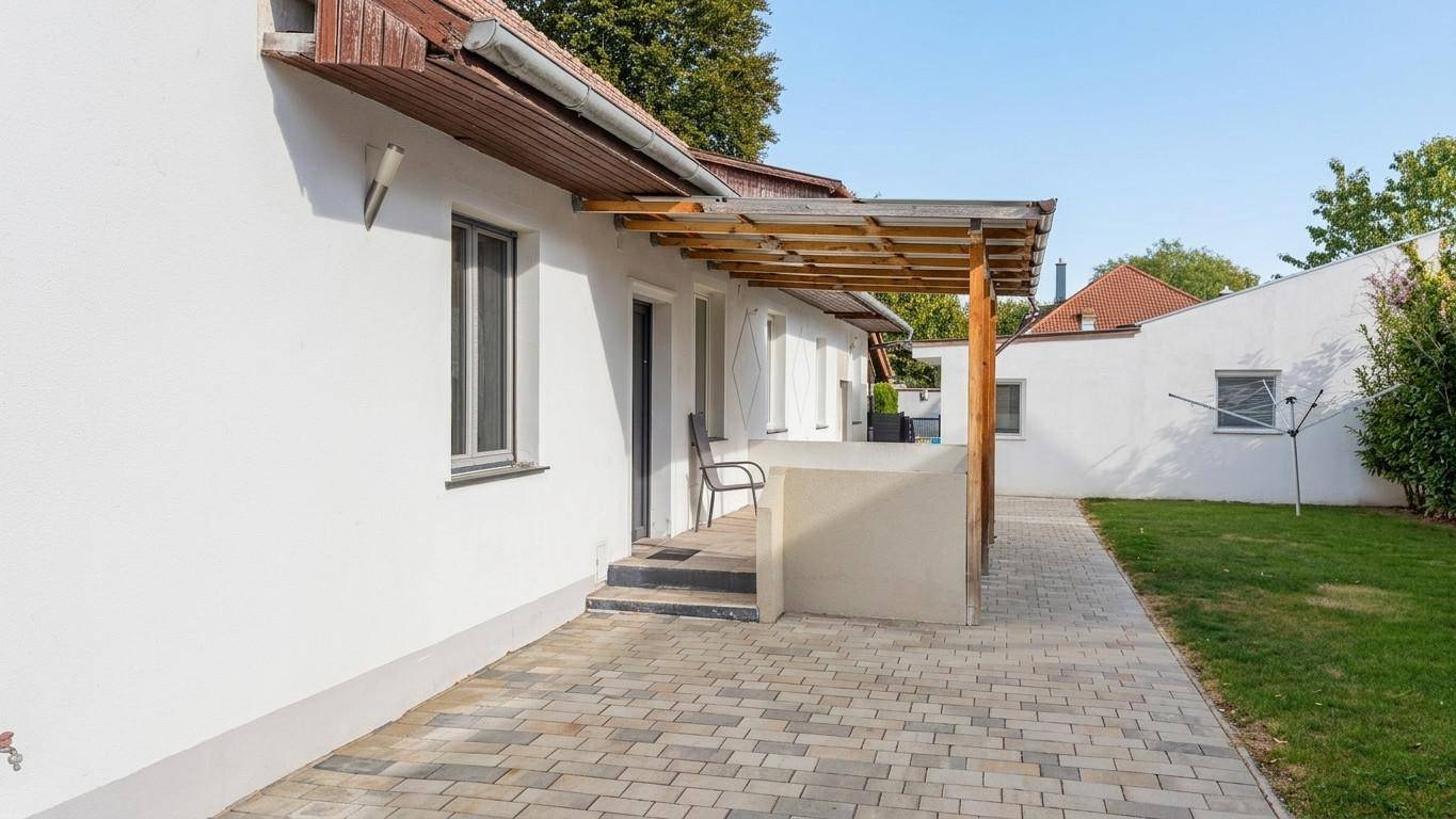 Gepflasterter Terrassenbereich am Haus mit kleiner Überdachung und Zugang zum Garten.