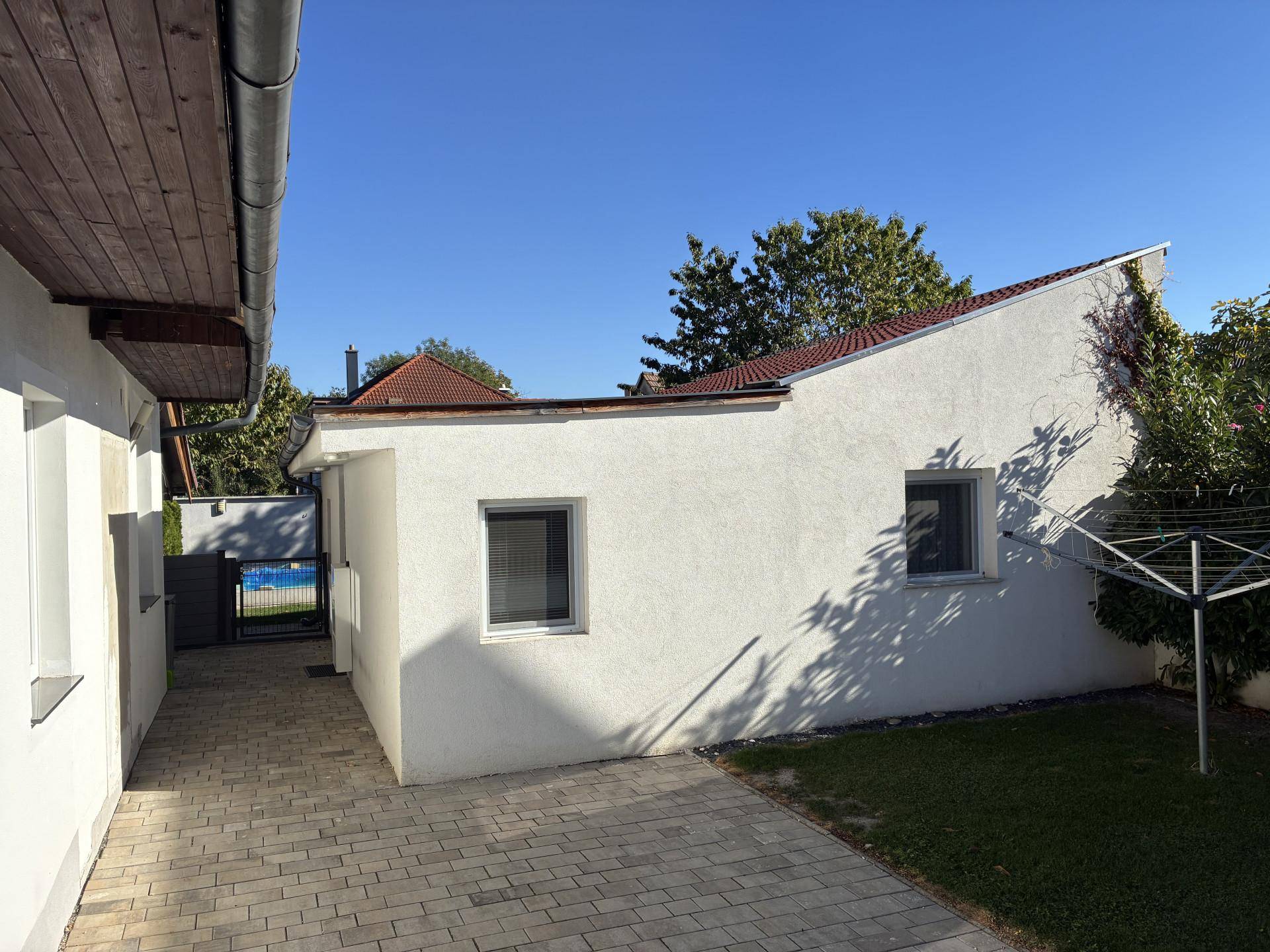Seitenansicht des Hauses mit gepflastertem Weg, Rasenfläche und sonnigem Himmel.