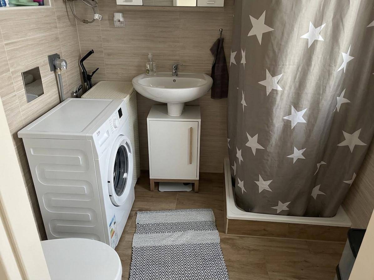 Kleines Badezimmer mit Dusche, Waschbecken und Waschmaschine.
