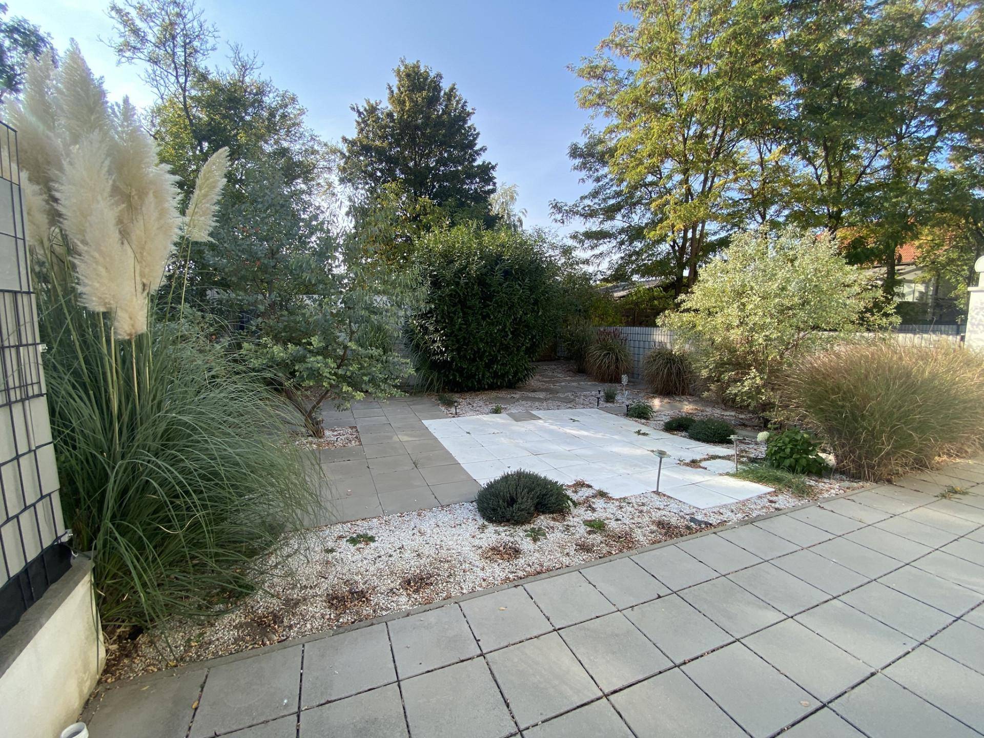 Gepflegter Gartenbereich mit großer gepflasterter Terrasse und üppiger Bepflanzung.