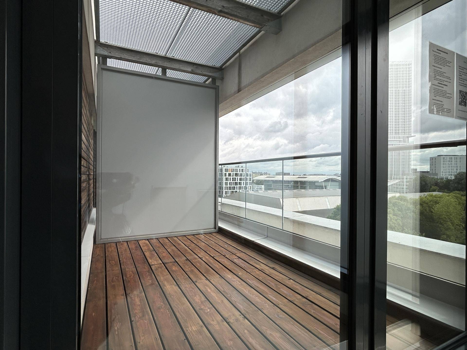 Heller Balkon mit Holzboden und Glasgeländer bietet einen weiten Blick auf die Stadt.