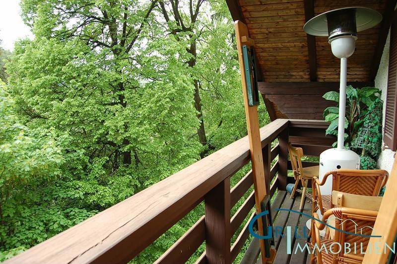 Gemütlicher Balkon mit Sitzgelegenheiten und einem Heizstrahler, umgeben von viel Grün und Bäumen.