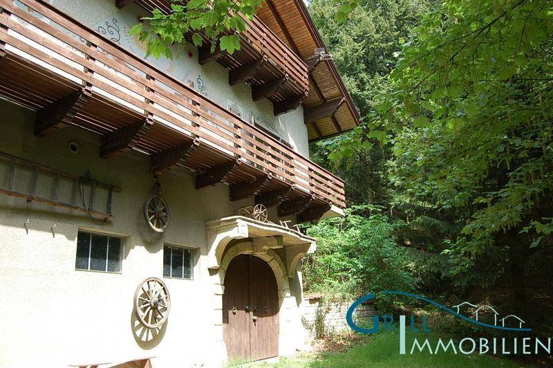 Seitenansicht des Hauses mit mehreren Holzbalkonen und traditionellen Verzierungen, umgeben von Bäumen.