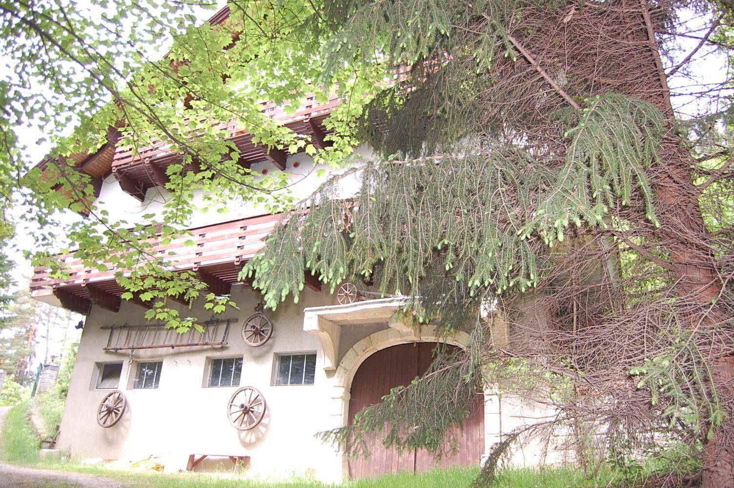 Traditionelles Haus mit Holzbalkonen, umgeben von üppiger Vegetation und hohen Bäumen.
