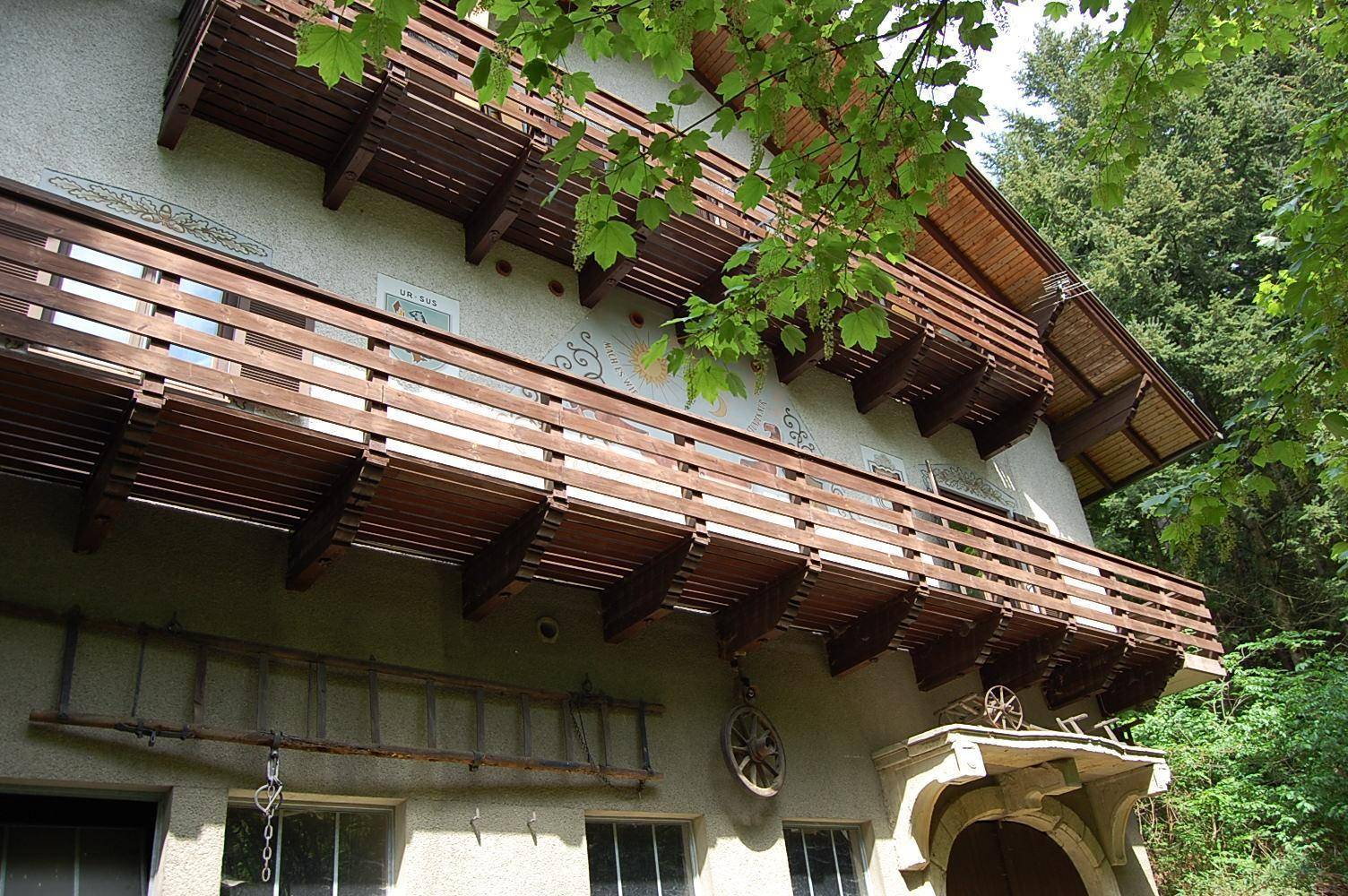 Seitenansicht des Hauses mit mehreren Holzbalkonen und traditionellen Verzierungen, umgeben von Bäumen.