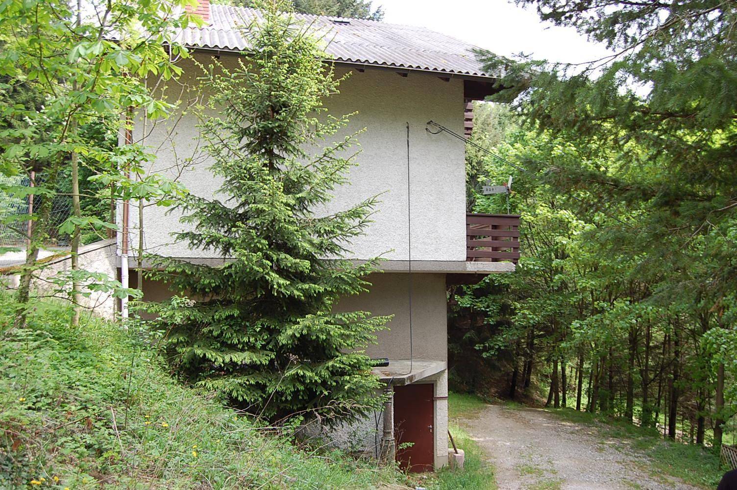 Rückseite des Hauses mit einfacher Fassade und umgebender Natur, eingebettet in eine grüne Landschaft.
