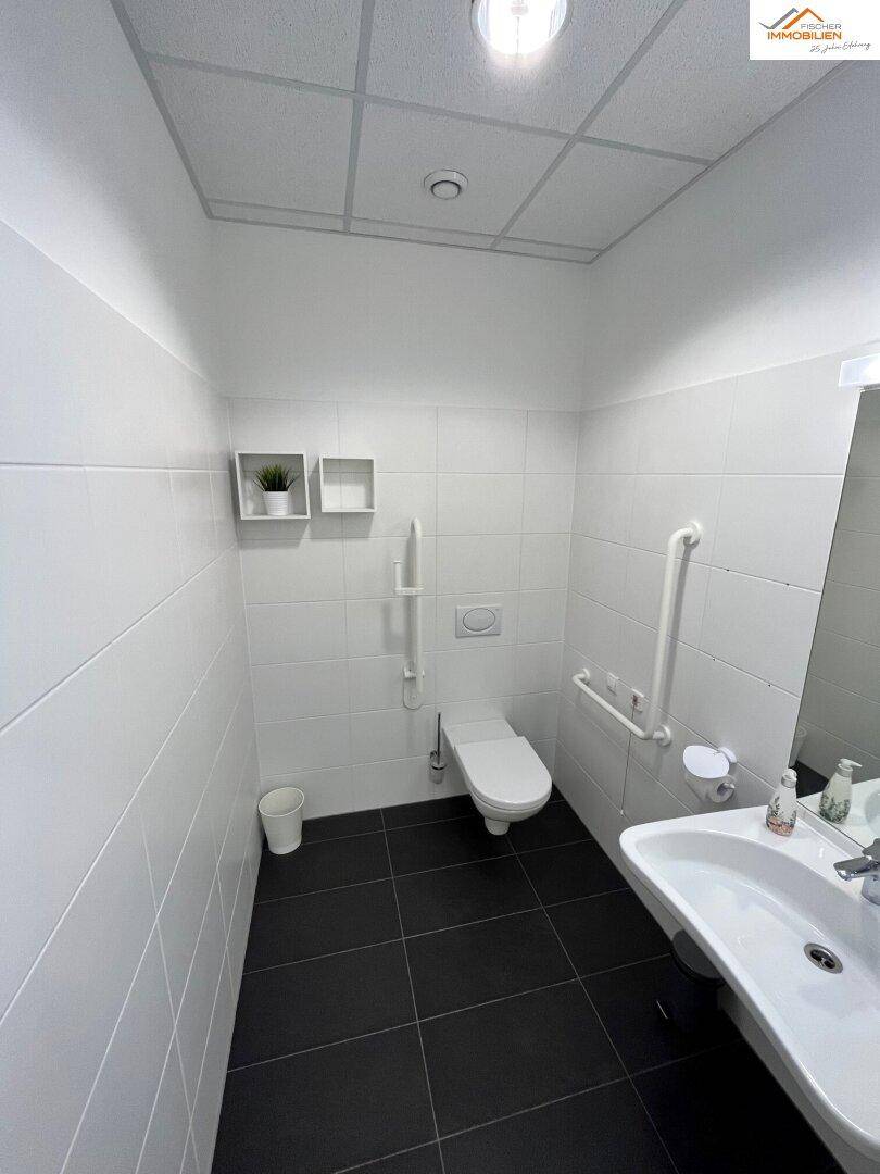 Barrierefreies Badezimmer mit Haltegriffen, wandhängendem WC und Waschbecken.