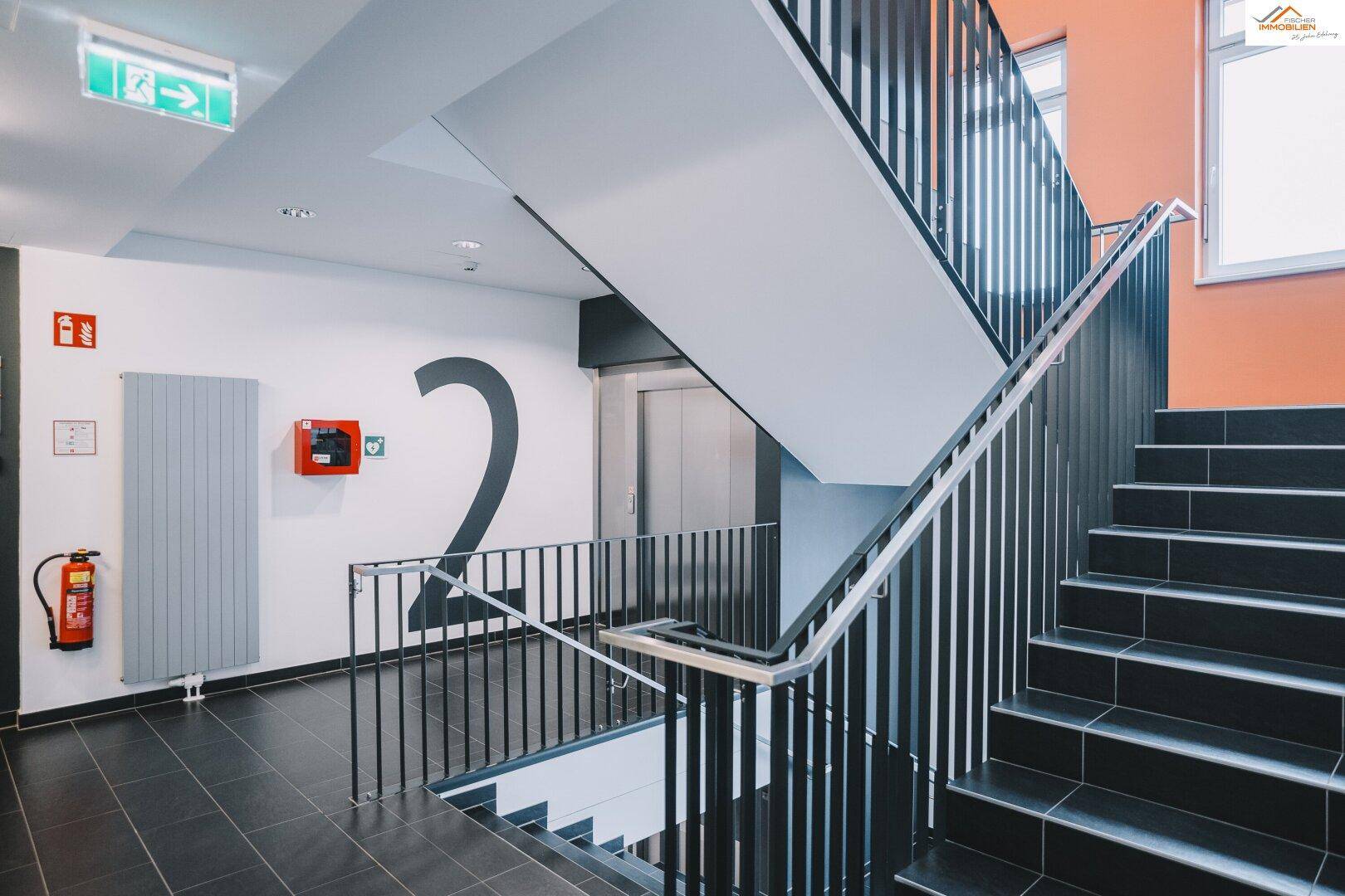 Modernes Treppenhaus mit dunklen Stufen, Metallgeländer und einem Aufzug.