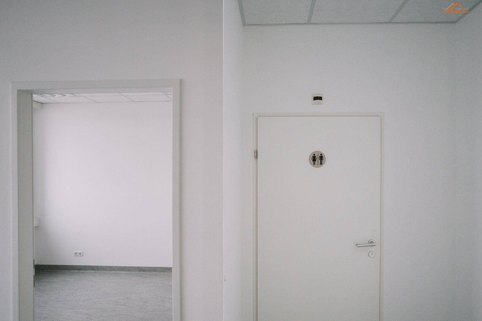 Flur mit zwei Türen, eine davon führt zu den Toiletten, gekennzeichnet mit Piktogrammen.