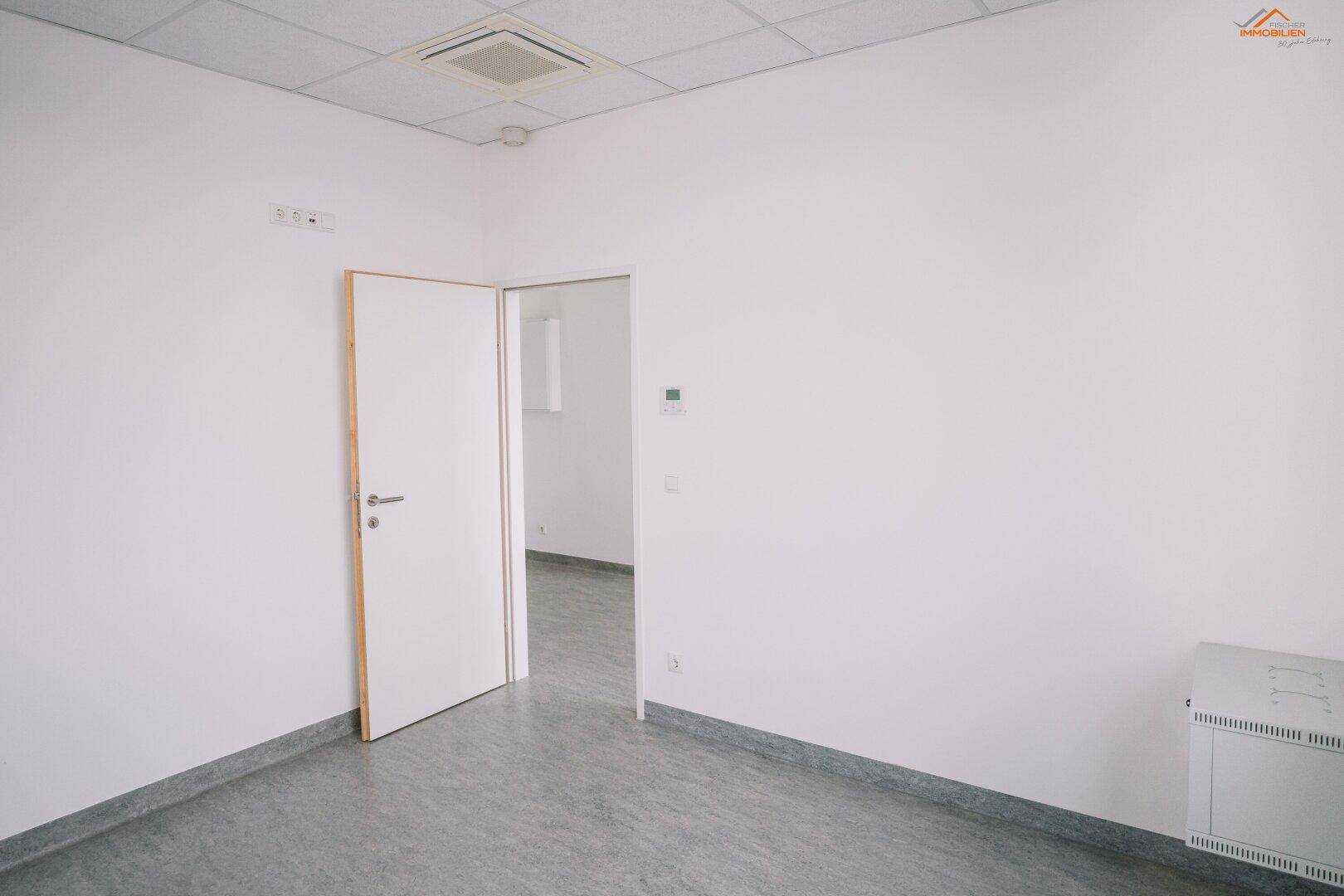 Leerer Büroraum mit Heizkörper und offener Tür zu einem weiteren Bereich.