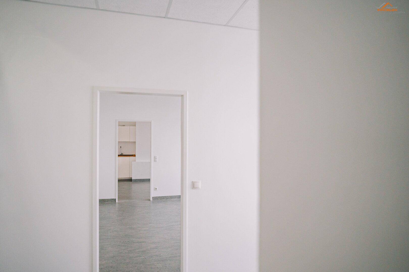 Blick durch eine offene Tür in einen Raum mit einer sichtbaren Küchenzeile im Hintergrund.