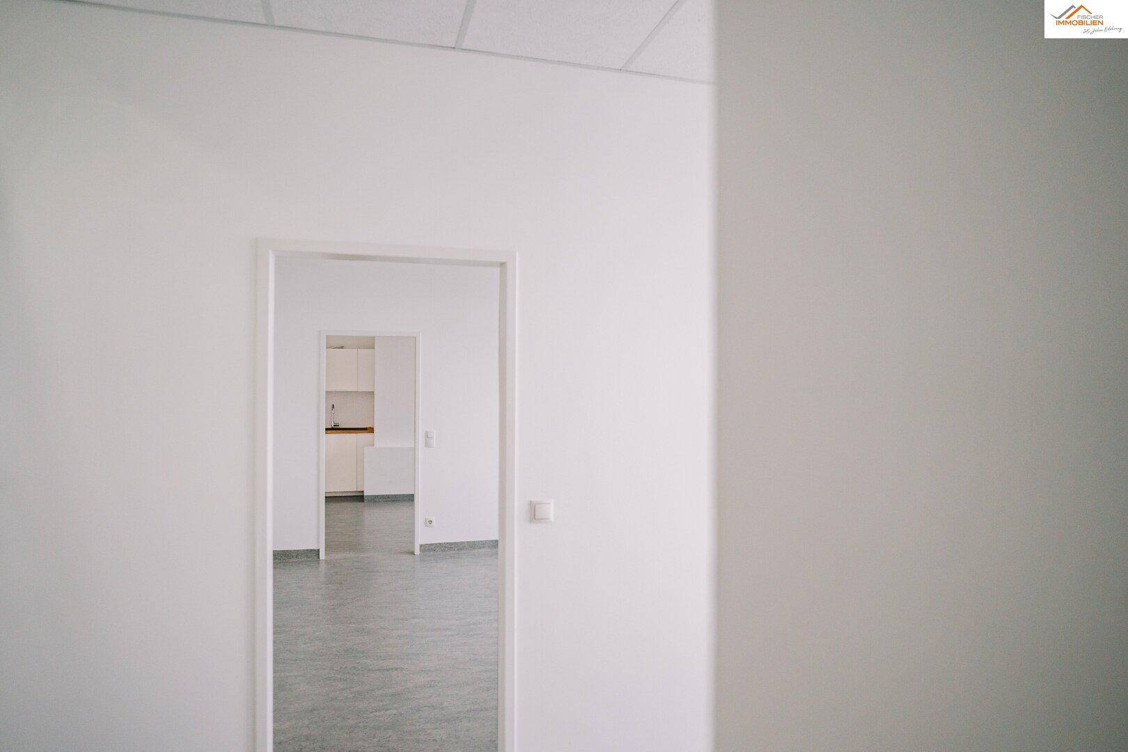Blick durch eine Tür in einen hellen, leeren Raum mit Küchenzeile.