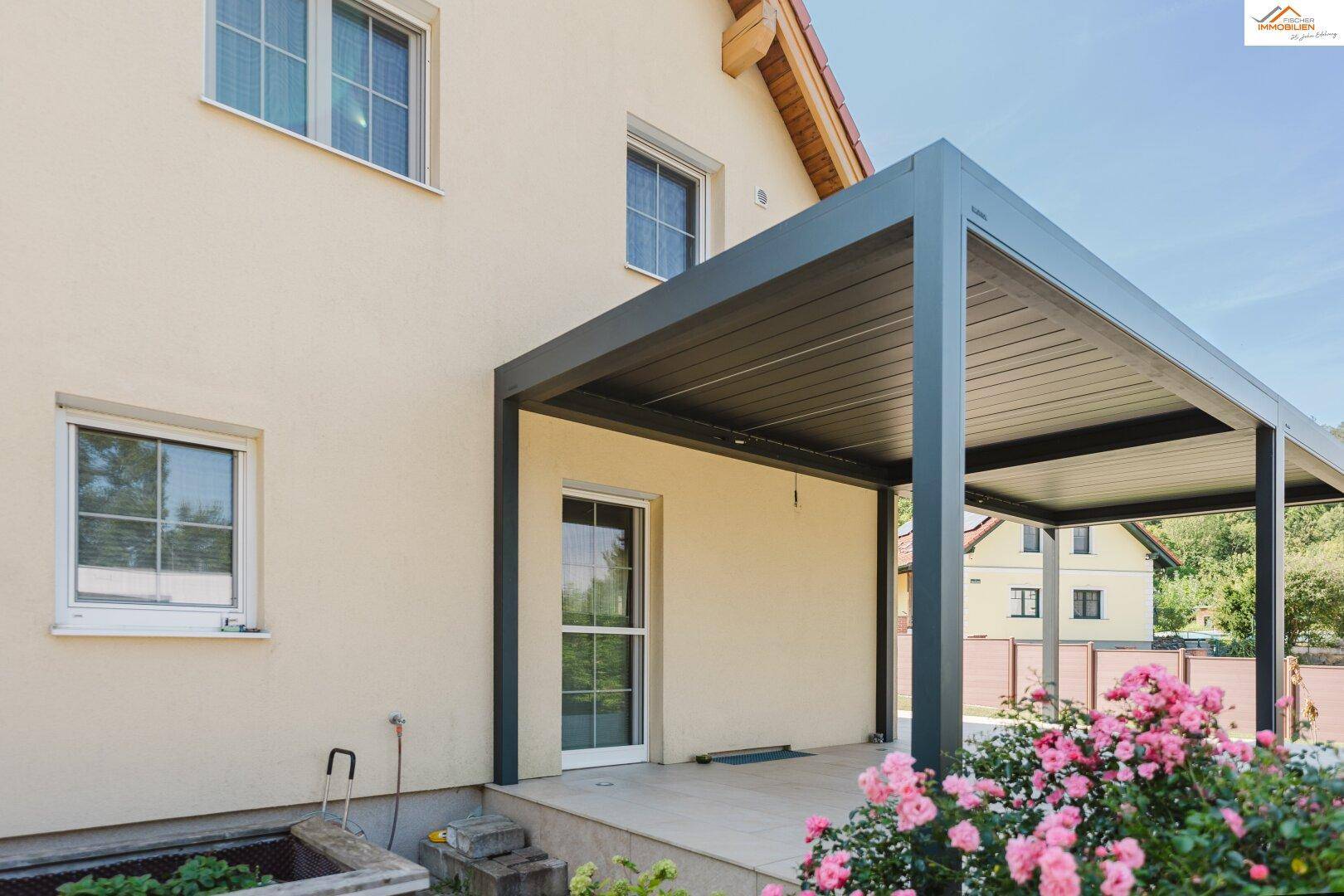 Detailansicht der überdachten Terrasse mit blühenden Rosen im Vordergrund.