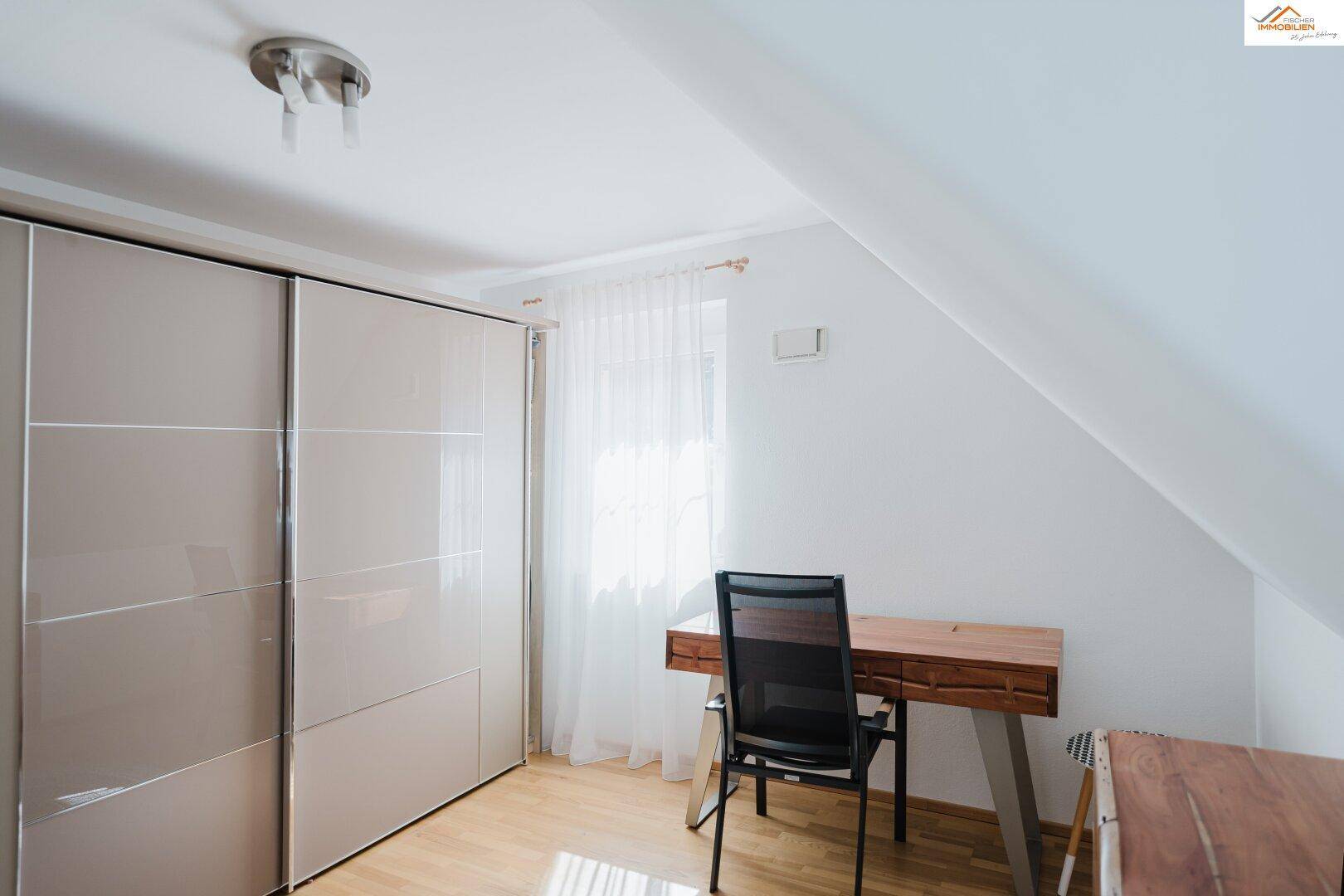 Schlafzimmer oder Arbeitszimmer mit Schreibtisch, Schiebetürenschrank und Dachschräge.