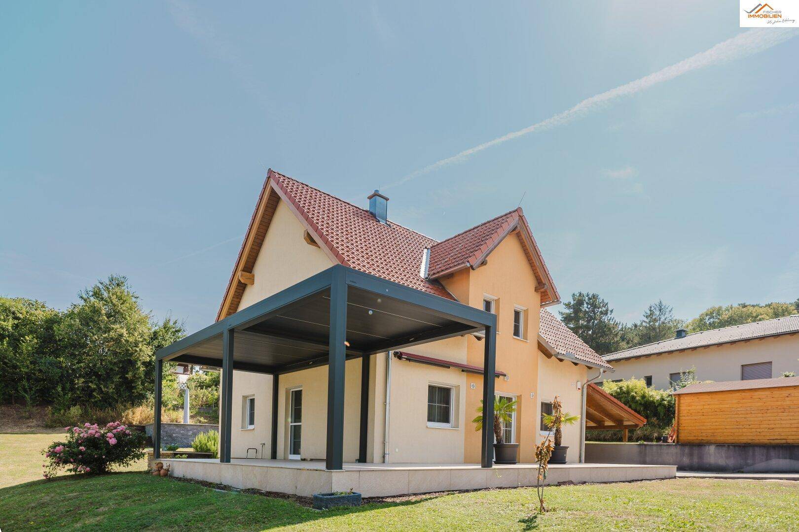 Seitenansicht des Hauses mit überdachter Terrasse und gepflegtem Rasenbereich.