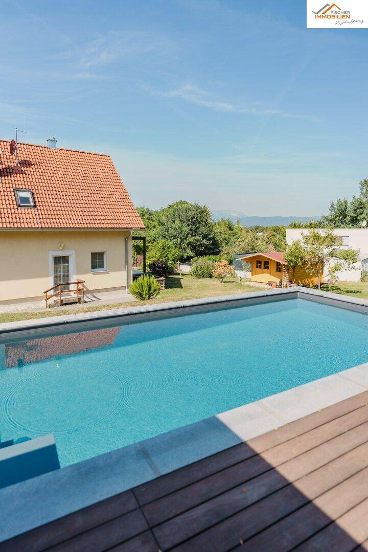 Außenbereich mit großem Pool, Holzdeck und Blick auf das Wohnhaus und die umliegende Natur.
