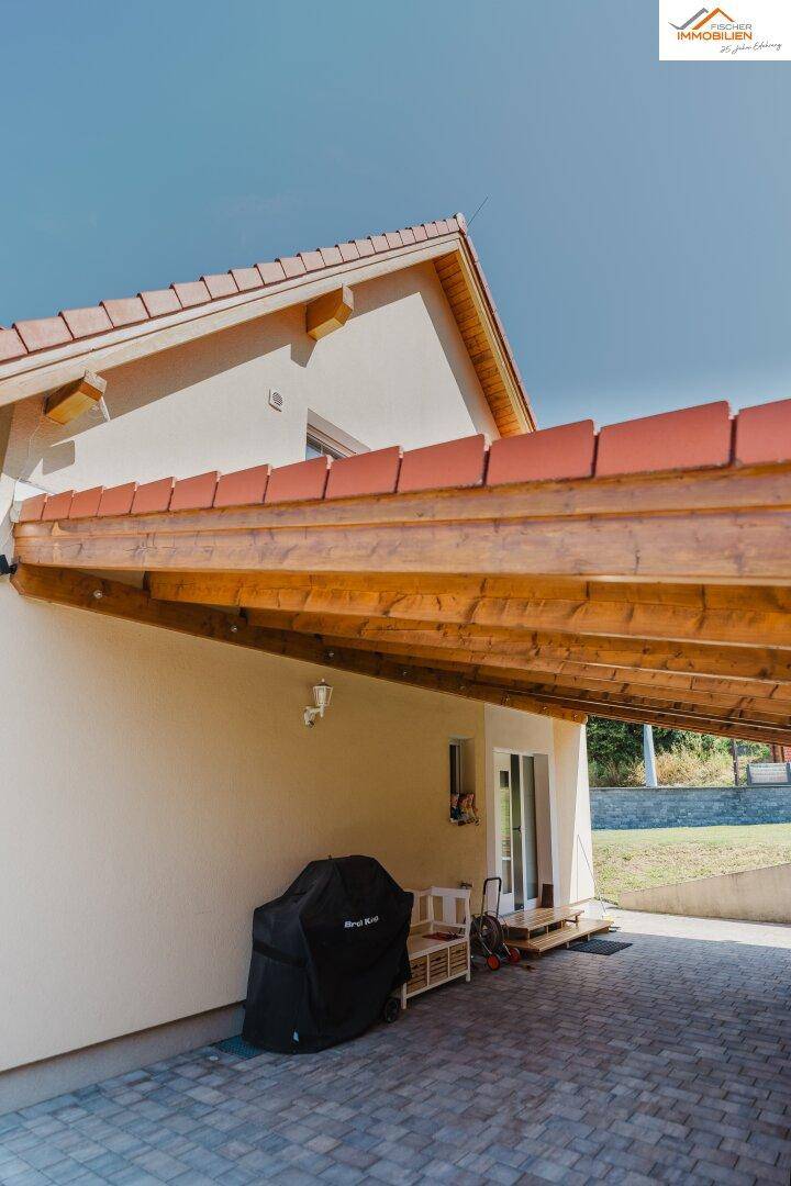Überdachter Carportbereich neben dem Haus mit Grillplatz und Zugang zum Garten.