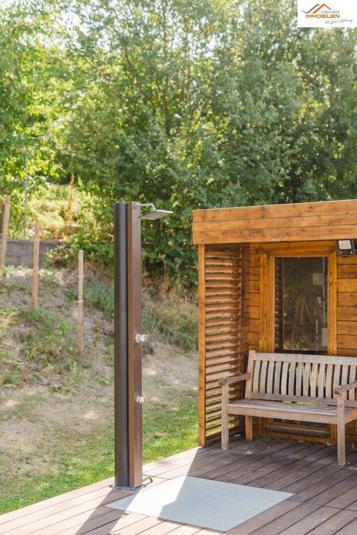 Außendusche und Holzbank neben einem kleinen Holzhaus, umgeben von viel Grün.