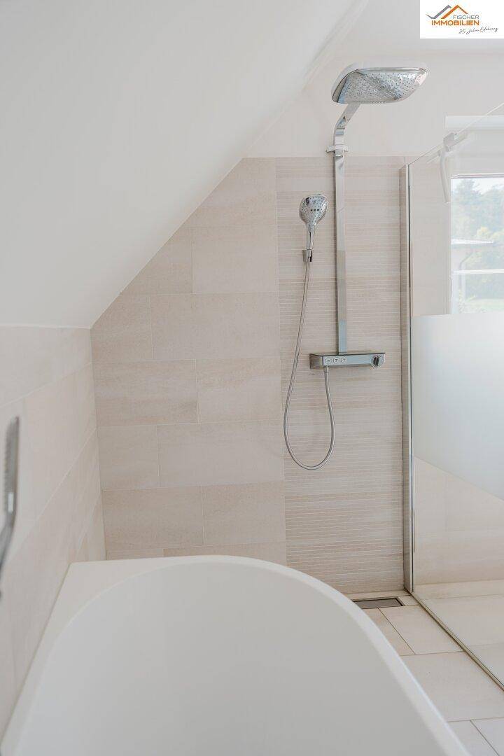 Modernes Badezimmer mit Dusche, Badewanne und hellen Fliesen unter der Dachschräge.