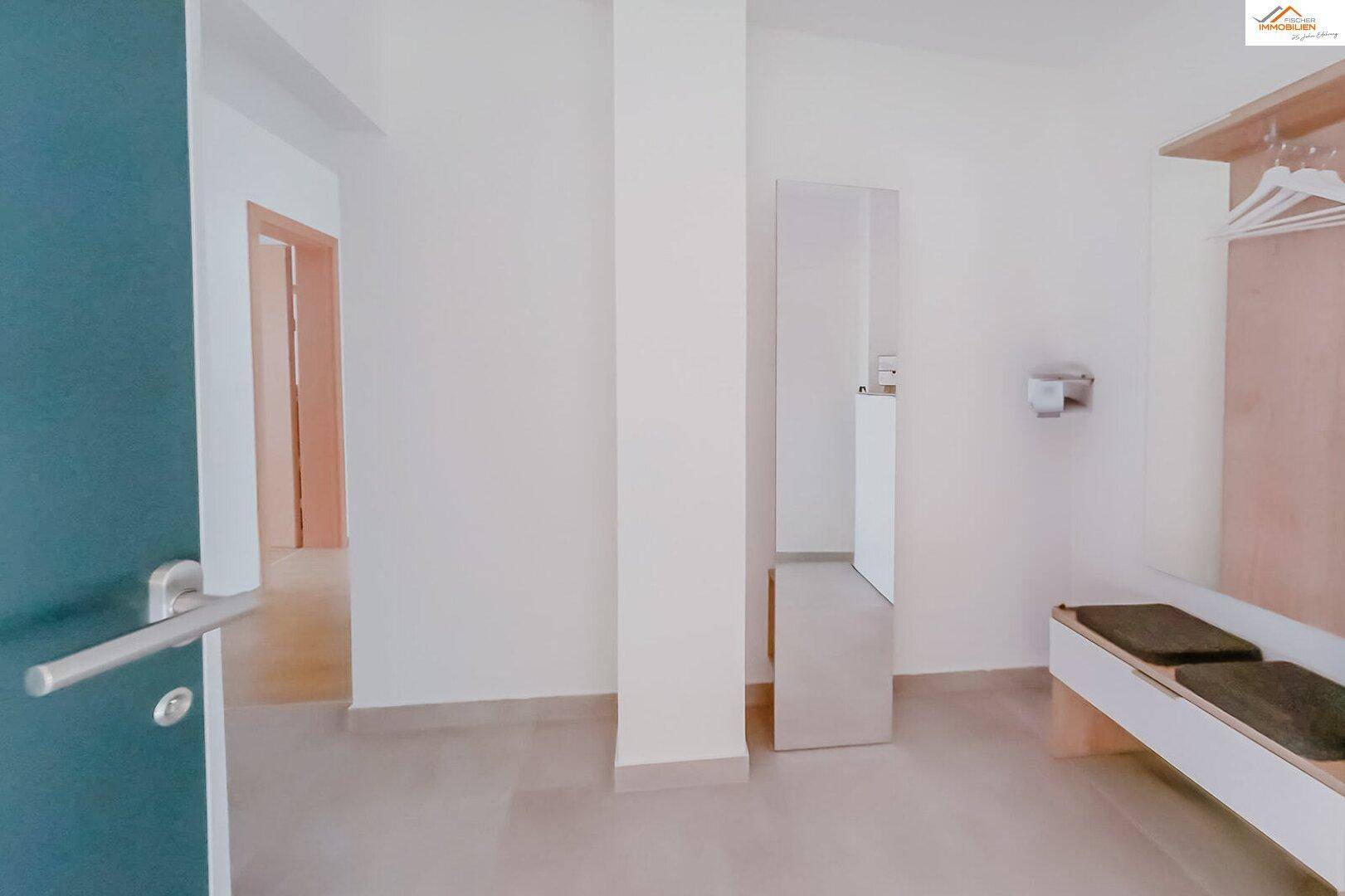 Heller Eingangsbereich mit Garderobe, Sitzbank und großem Spiegel.