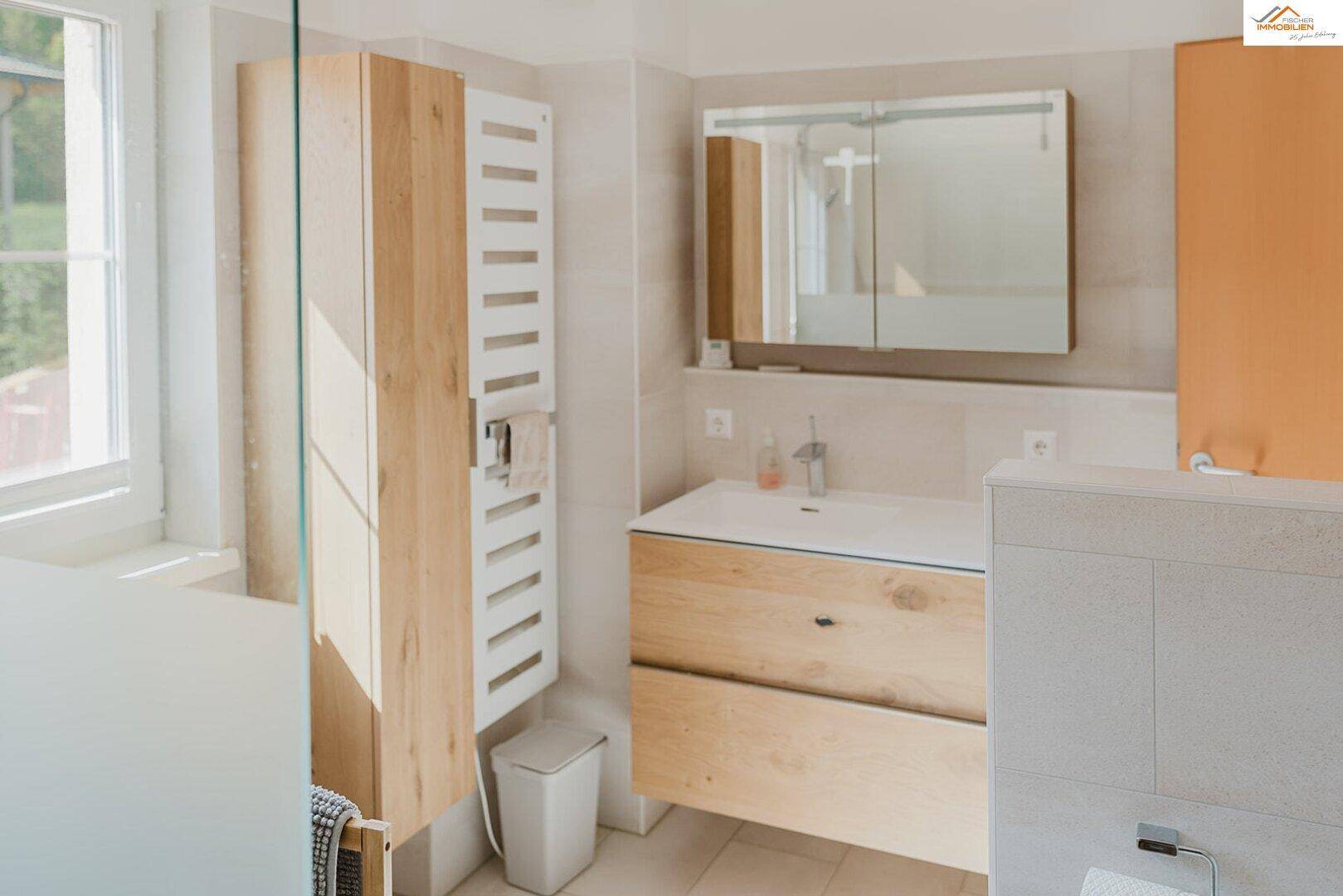 Badezimmer mit Holzwaschtisch, Spiegelschrank, Handtuchheizkörper und Fenster.