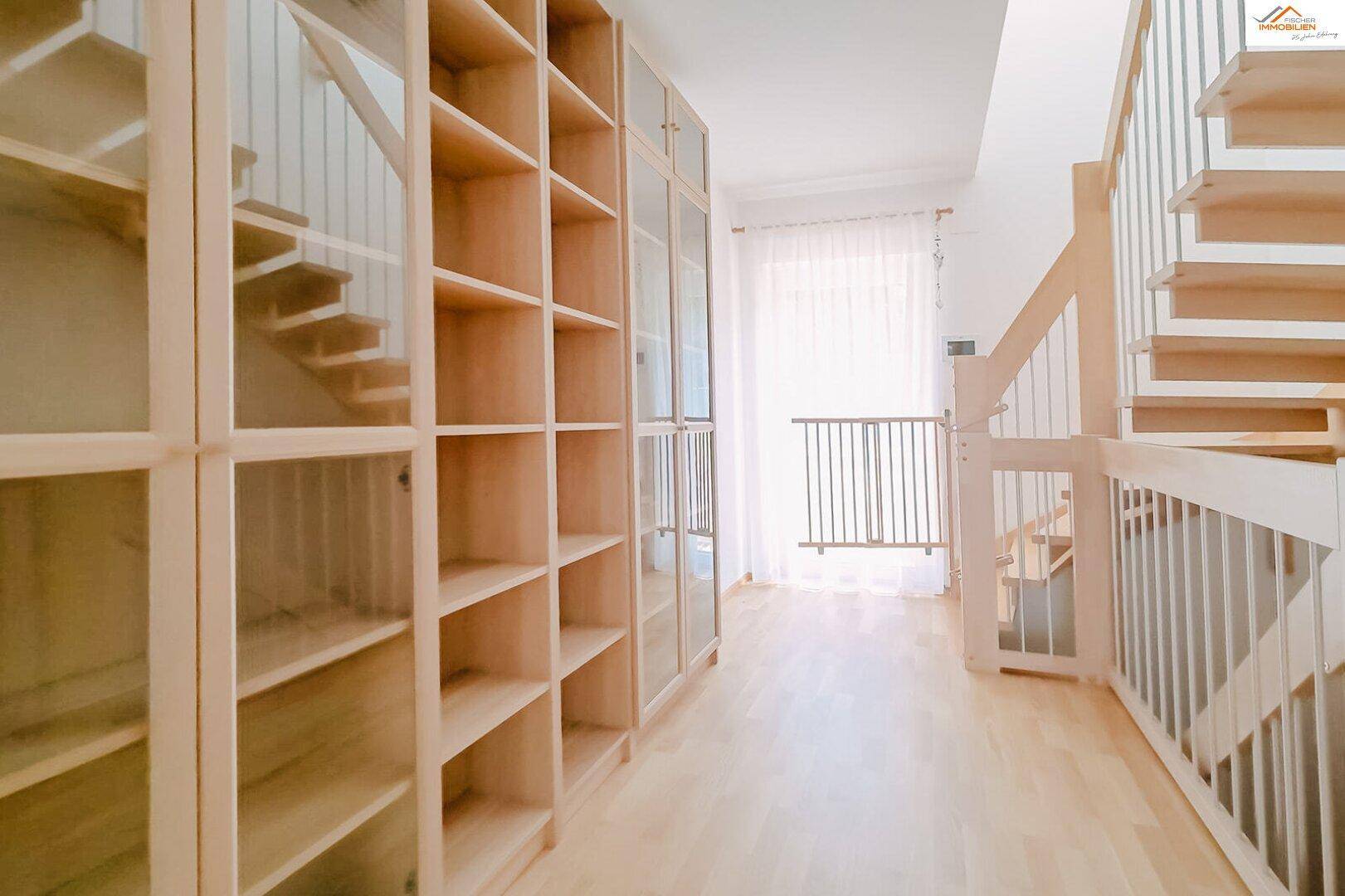 Heller Flur mit Holztreppe und integrierten Bücherregalen aus hellem Holz.