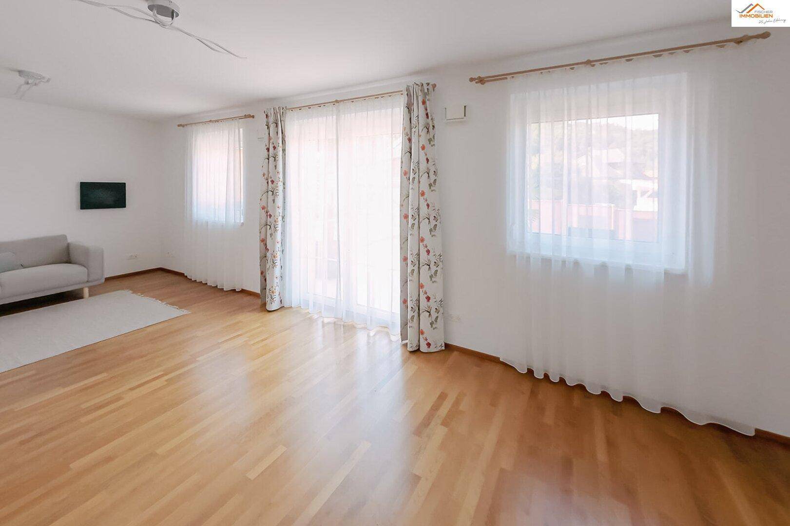 Helles Wohnzimmer mit Holzparkettboden, großen Fenstern und Zugang zum Außenbereich.