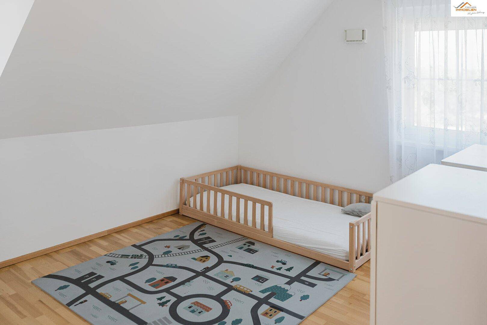 Kinderzimmer mit kleinem Holzbett, Spielteppich und Dachschräge.