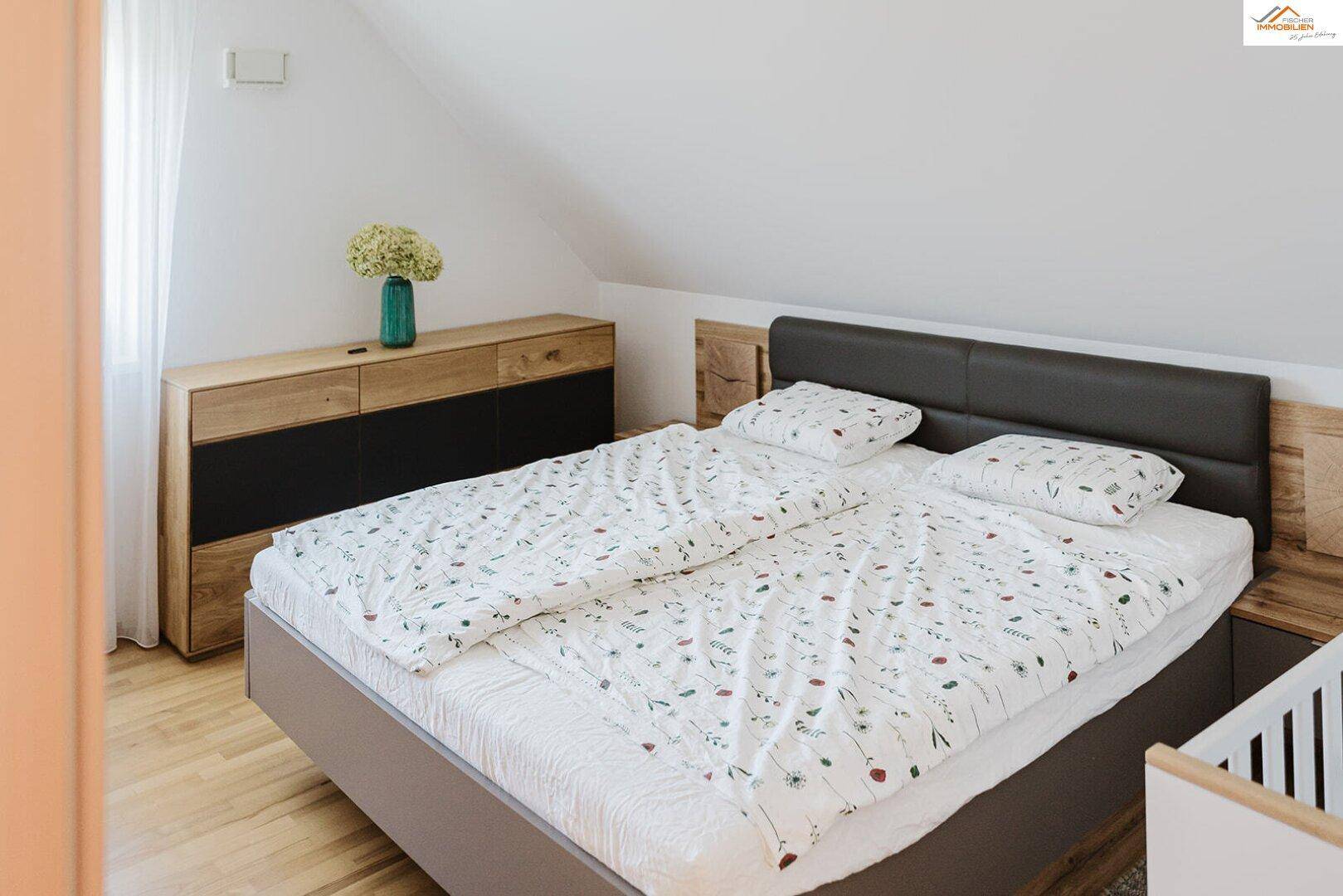 Helles Schlafzimmer mit Doppelbett, Holzkommode und Fenster mit Blick ins Grüne.